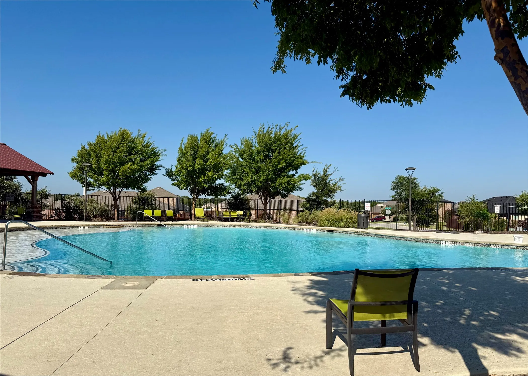 Outdoor swimming pool with concrete decking, metal handrails, and a covered patio area