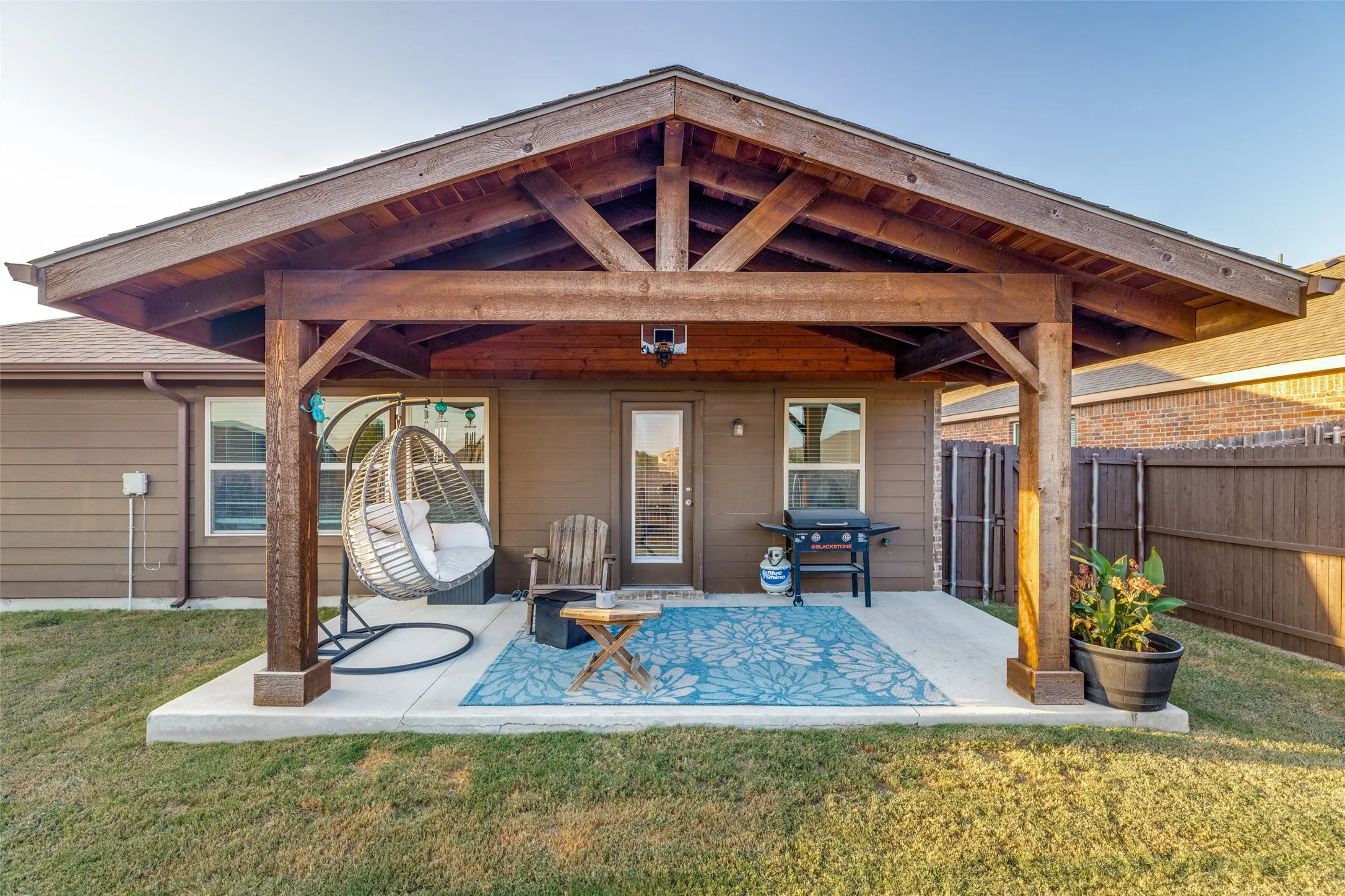 Covered outdoor patio with exposed beam ceiling, concrete flooring, and a flat-paneled privacy fence