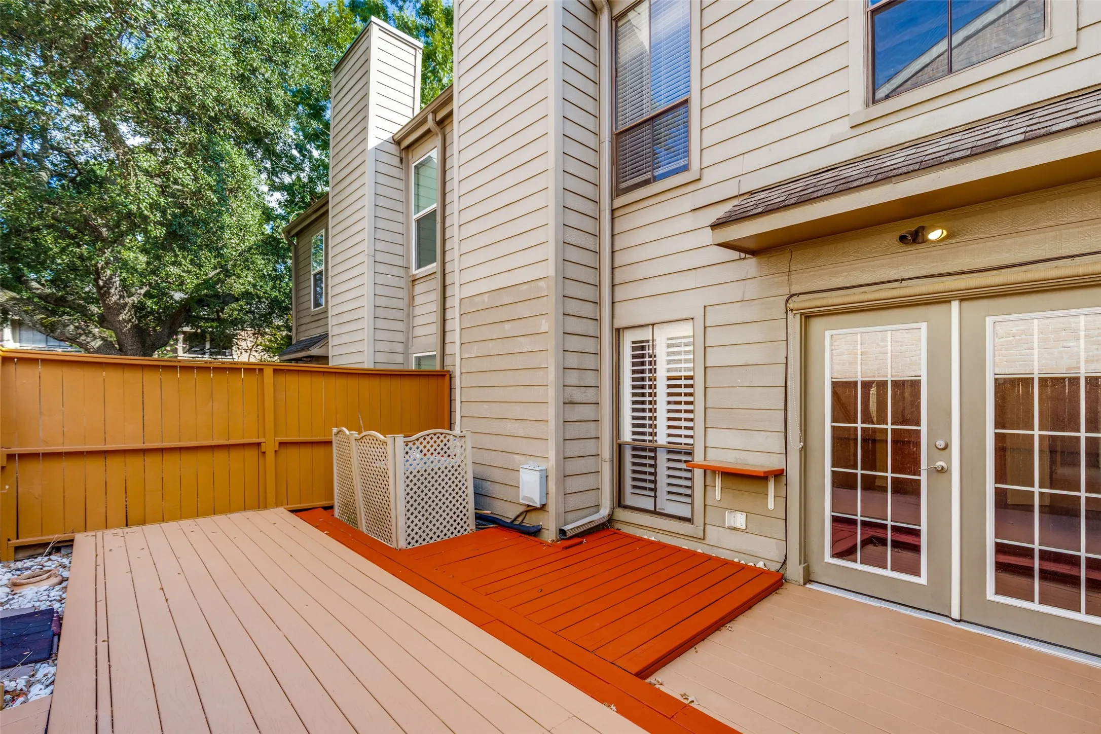 Expansive multi-level wood deck, privacy fencing, dual pane glass panel doors, and exterior wall sconce