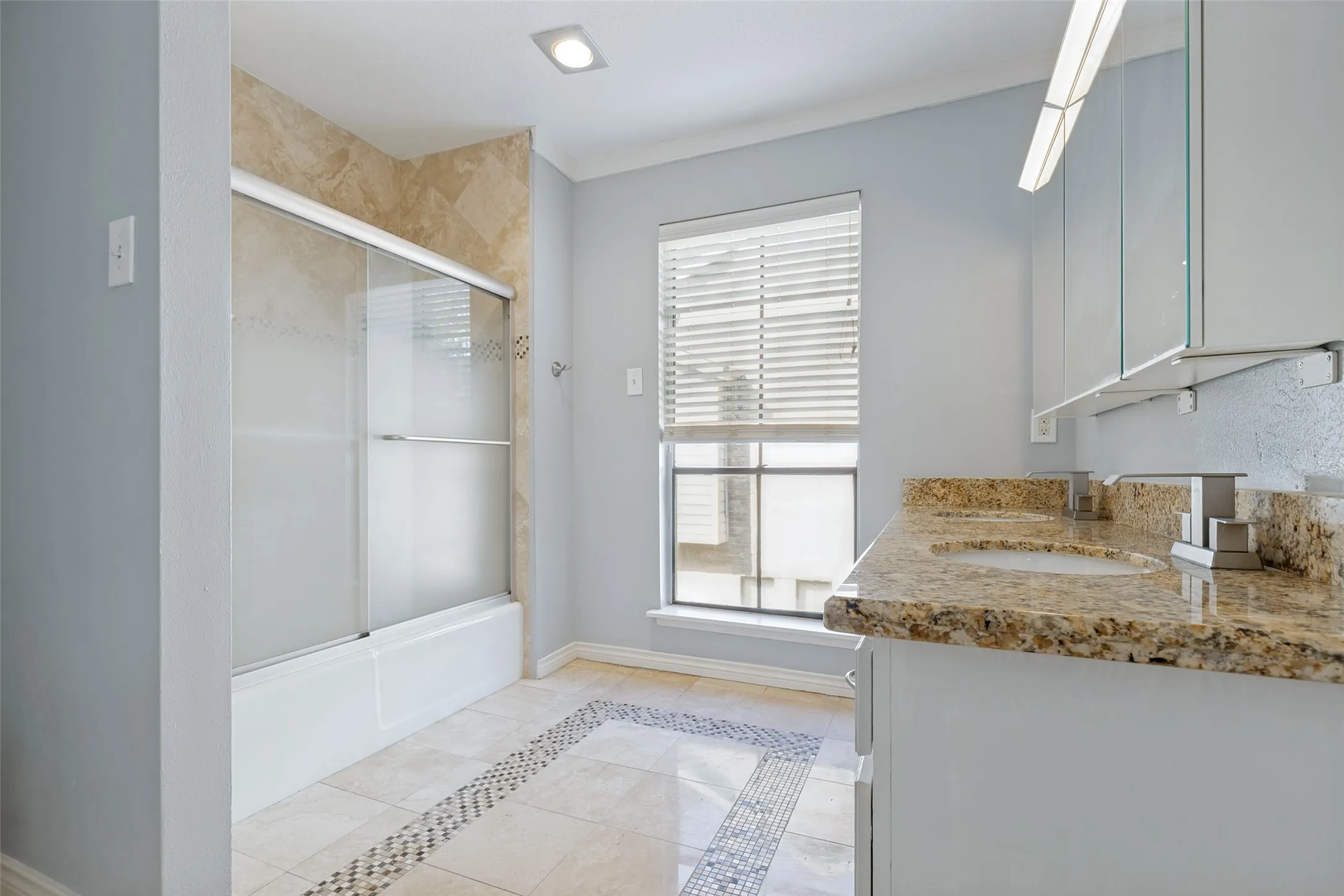 Dual vanity with stone countertop, tile flooring with decorative inlay, built-in bathtub with sliding glass doors, and recessed lighting