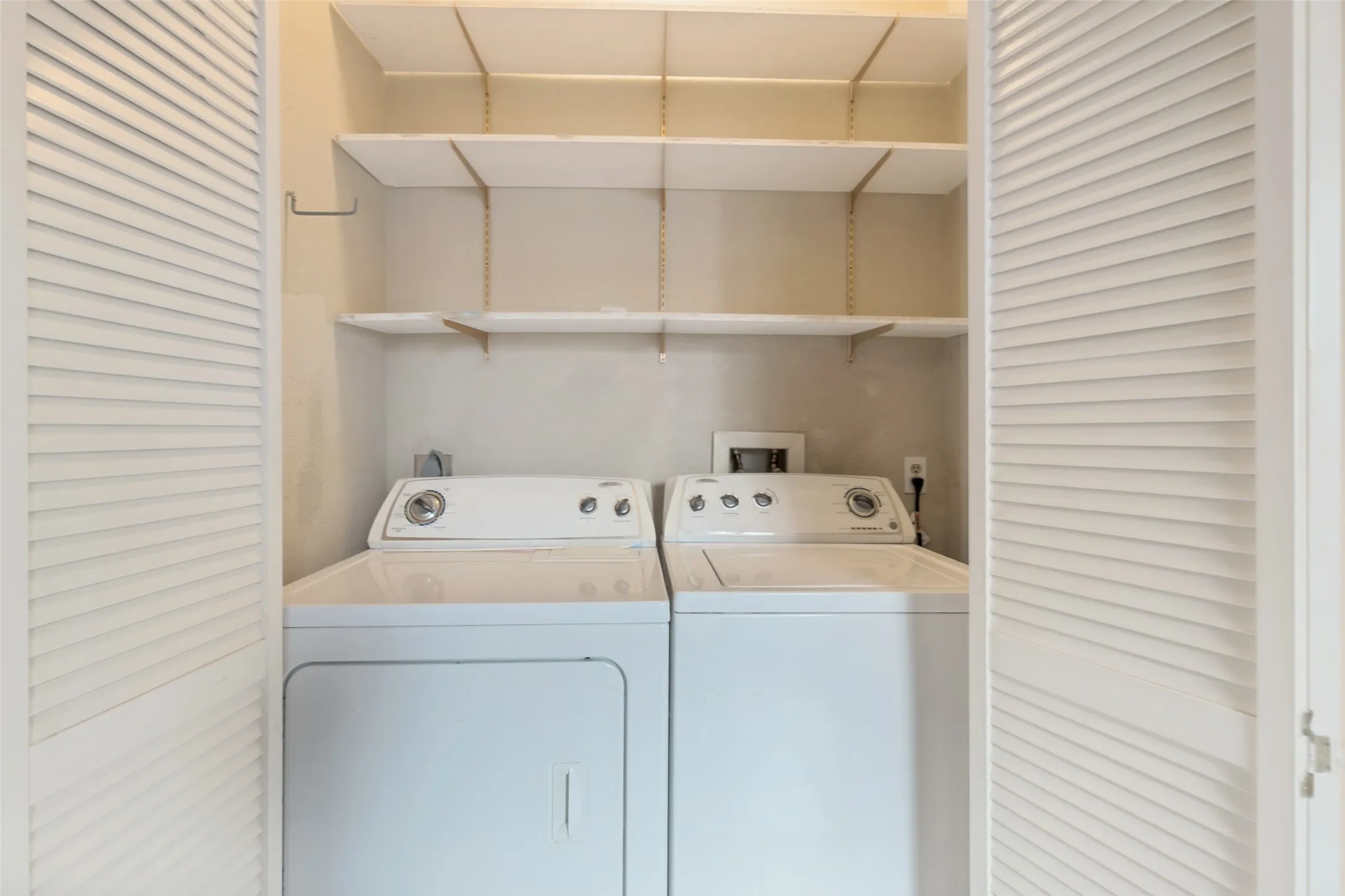 Louvered bifold doors opening to a laundry area with upper shelving