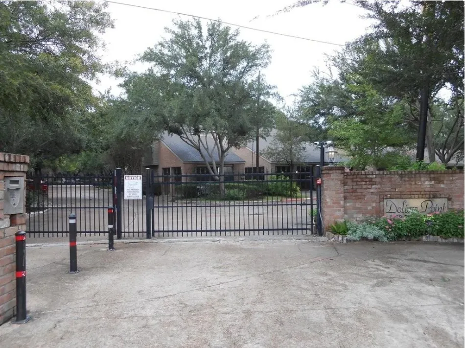 Brick entry column with a built-in mailbox, black metal security gate, brick wall with "Dolphin Point" signage, and established perimeter landscaping