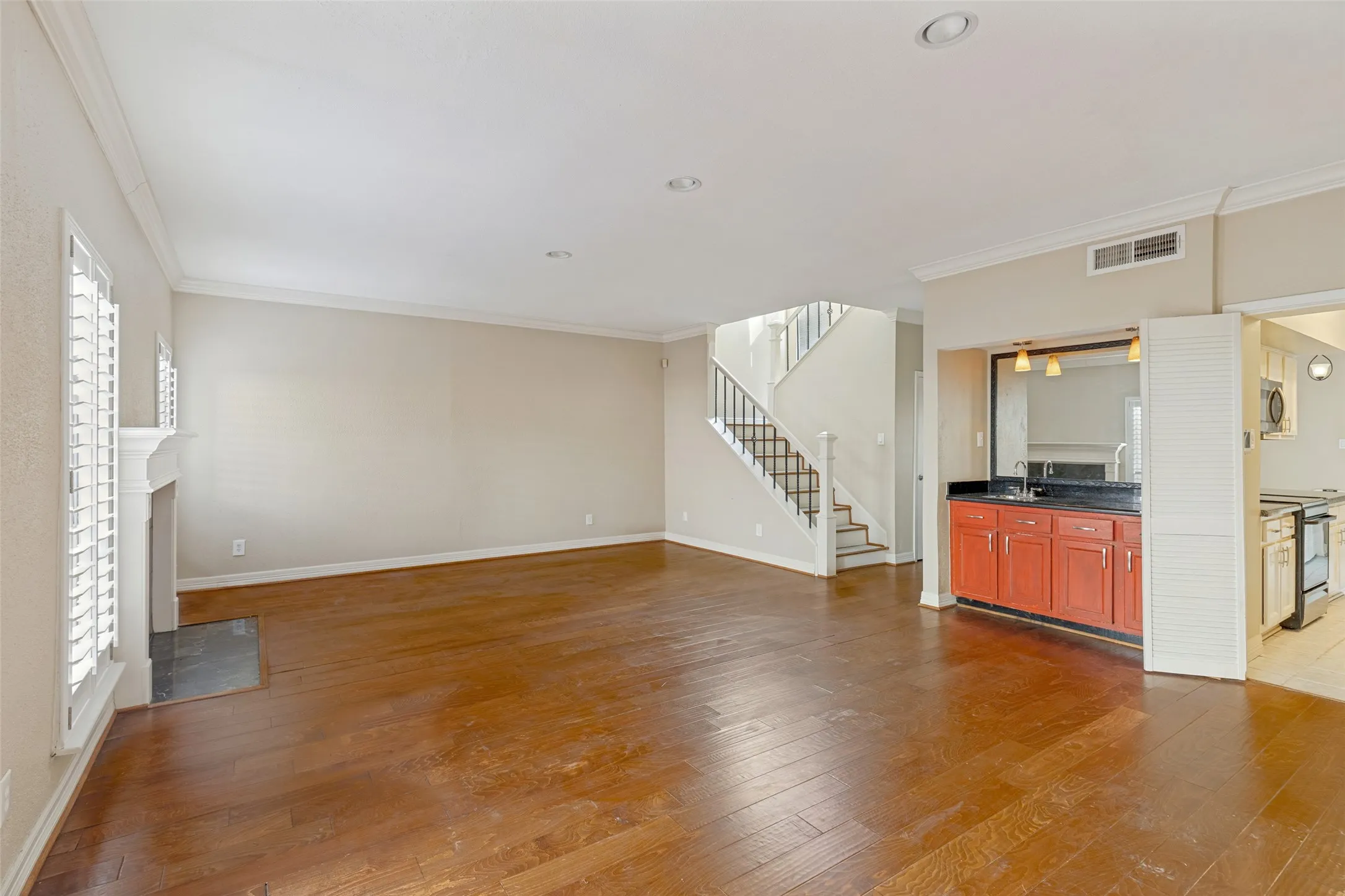 Wood-finish flooring, staircase with metal balusters, built-in wet bar with dark countertops, fireplace with stone surround, and crown molding