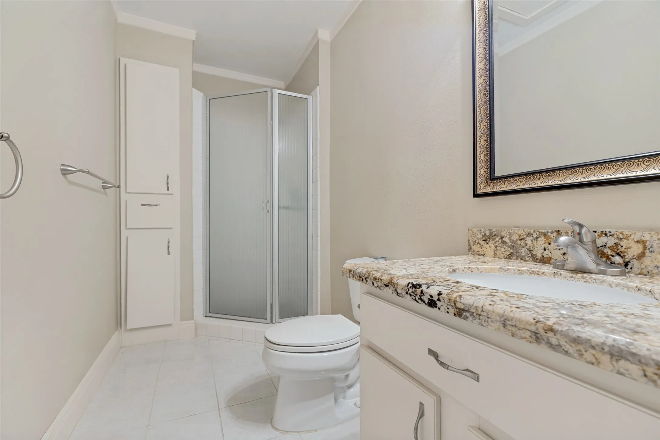 Built-in linen cabinet, glass-enclosed shower, vanity with stone countertop, drop-in sink, and framed mirror