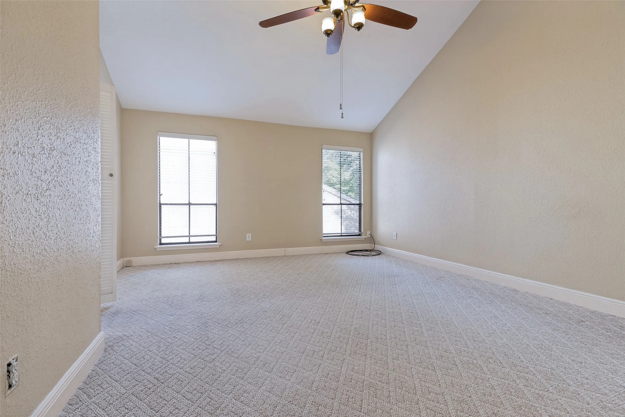 Vaulted ceiling with a ceiling fan, patterned carpet flooring, and two windows