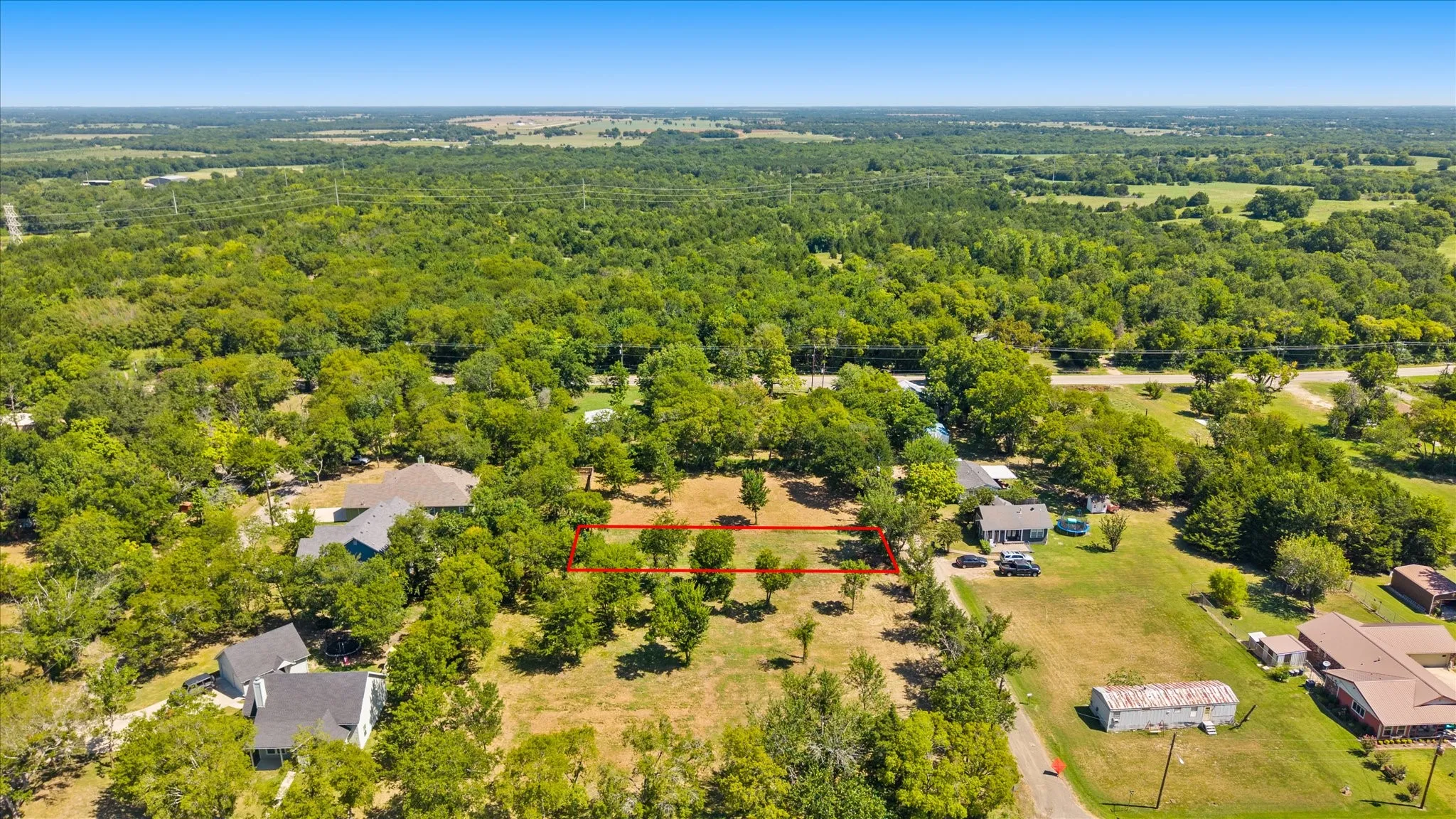 Expansive land parcel with surrounding mature trees and clear skies