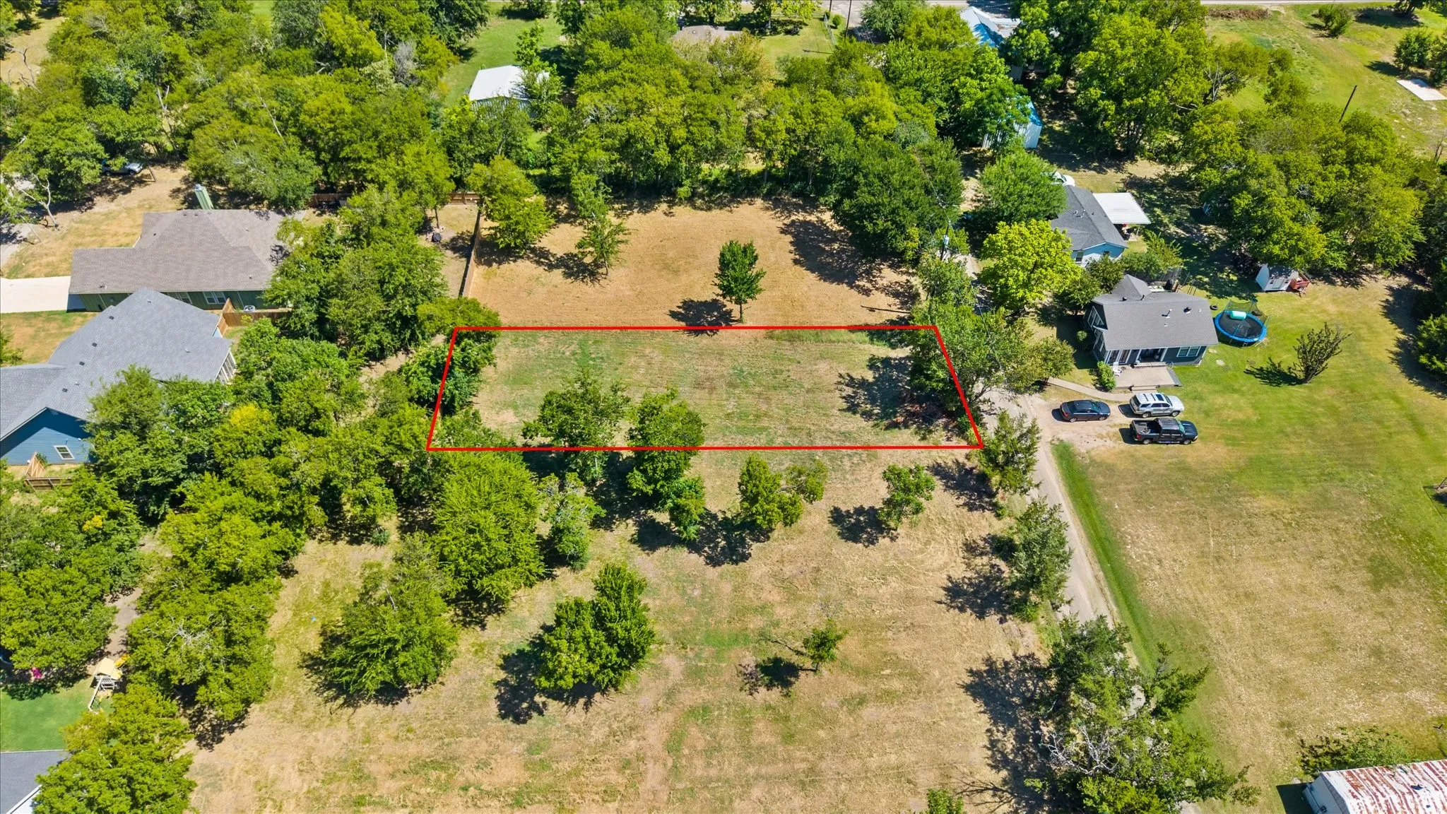 Expansive land lot featuring a clear building area, surrounding trees, and an open field
