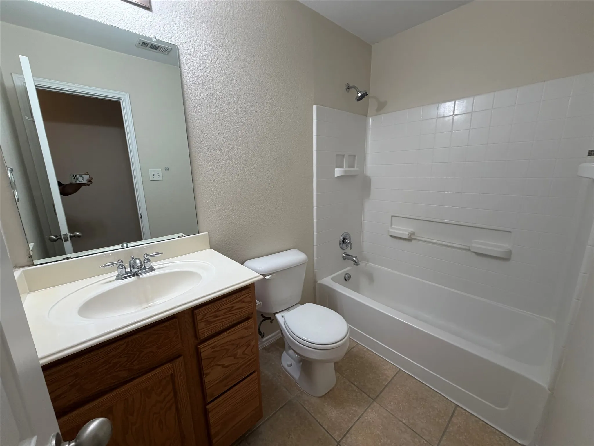 Bathroom featuring a built-in vanity with wood-finish cabinetry, a single basin sink, a large wall-mounted mirror, a tub/shower combination with a tiled surround, and ceramic tile flooring
