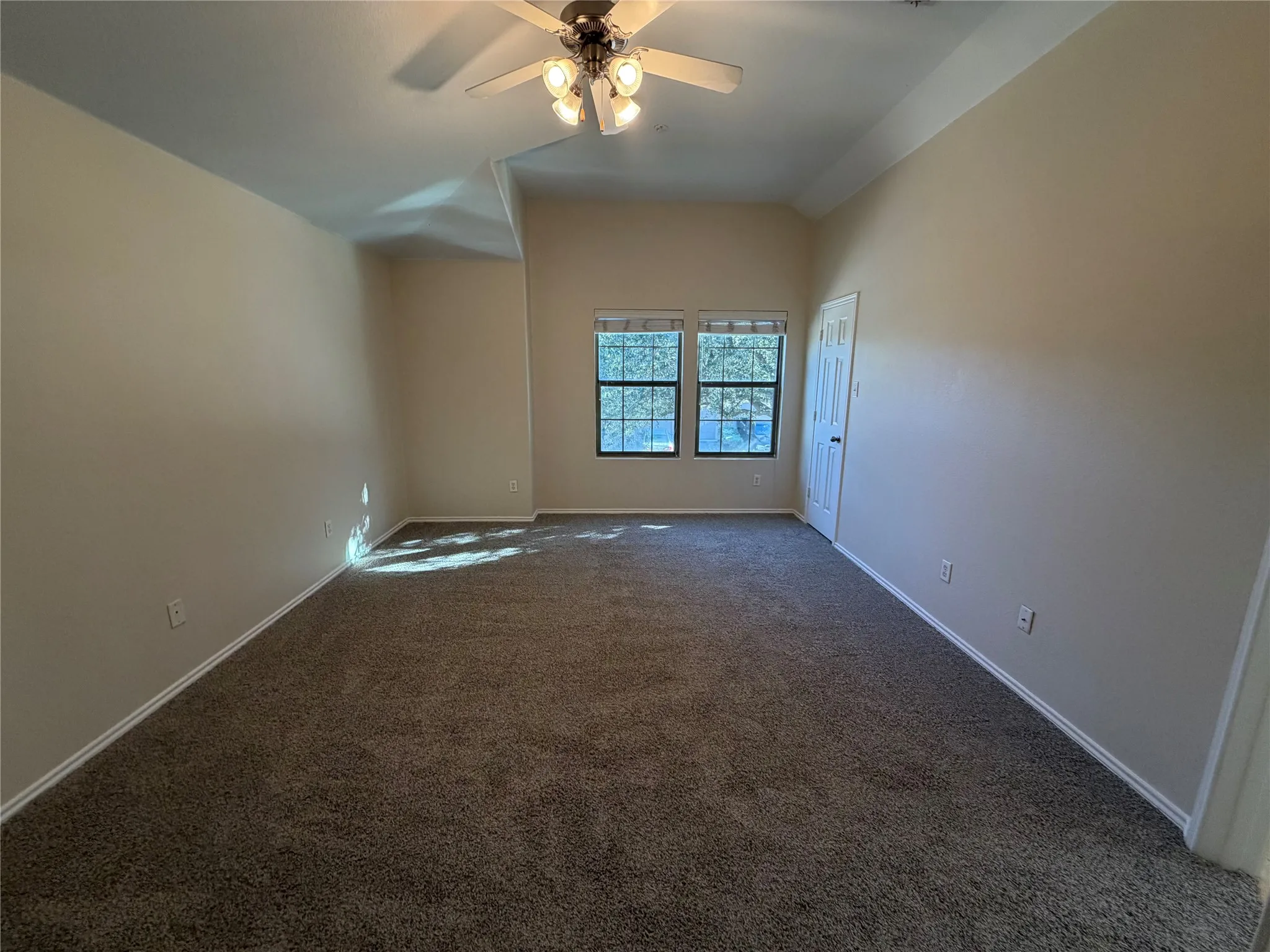 Spacious room featuring vaulted ceilings, neutral-toned walls, and plush carpet flooring