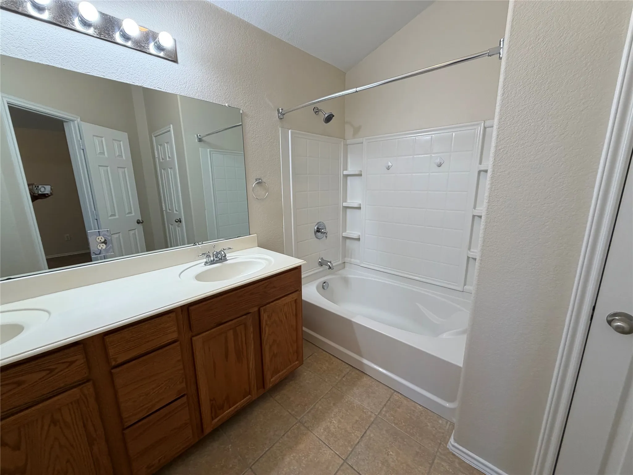 Double vanity with integrated sinks, wood-finish cabinetry, full-width mirror, and overhead strip lighting