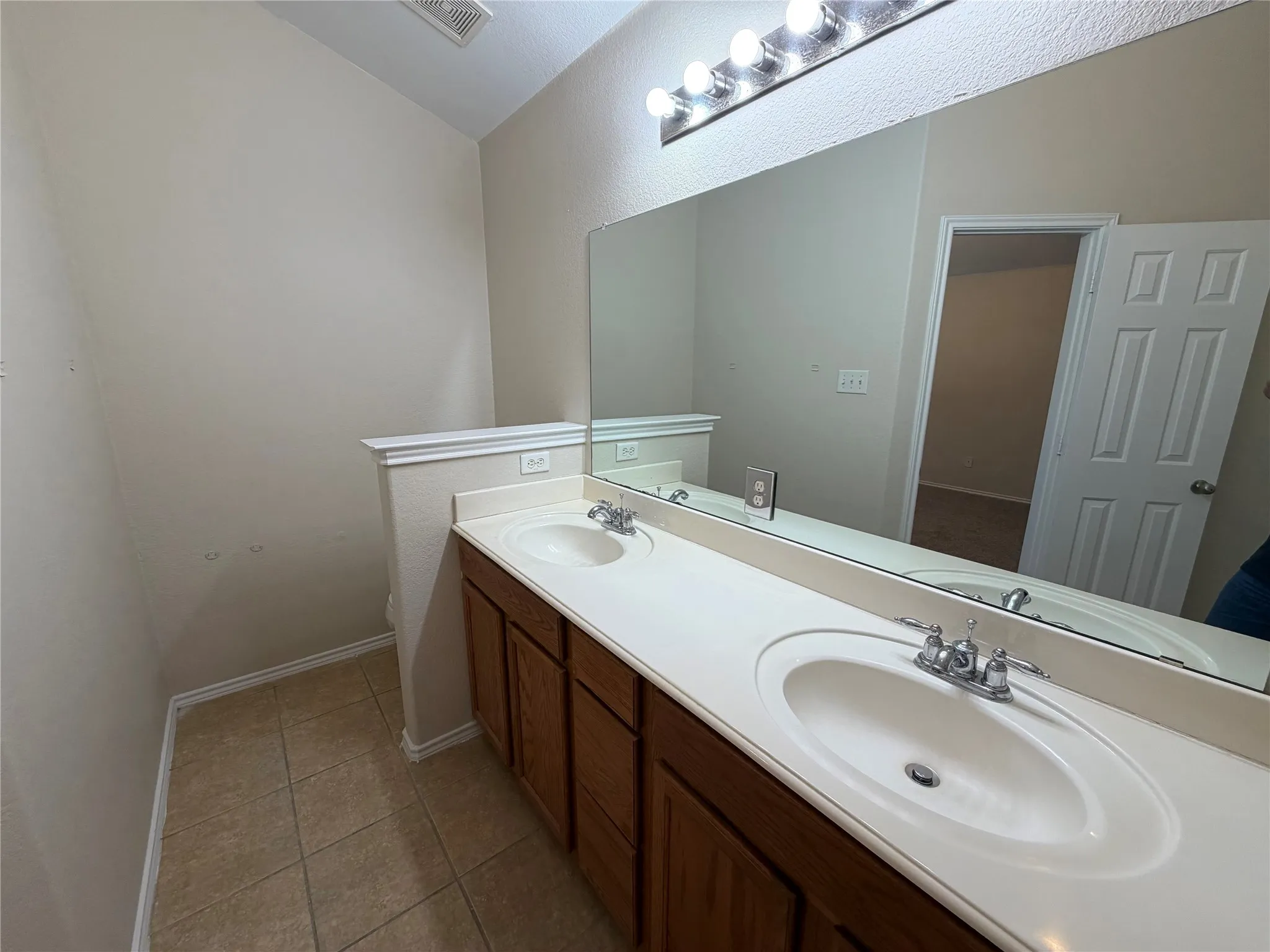 Dual vanity with integrated sinks, wood-finish cabinetry, a large wall-mounted mirror, and tile flooring