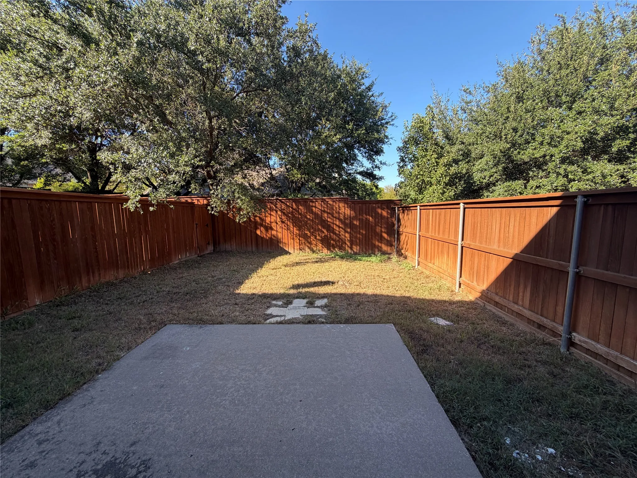 Private backyard with wood fencing, mature trees, and a concrete patio