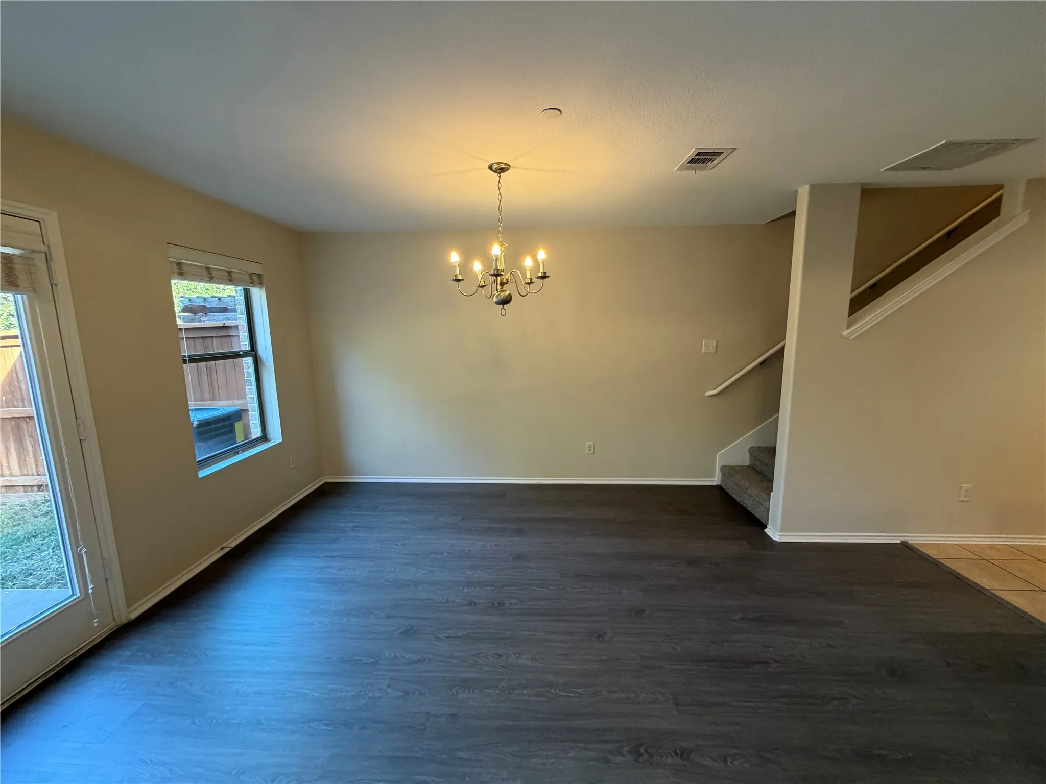 Dark wood-finish flooring with a chandelier, a window, and a glass-paneled door