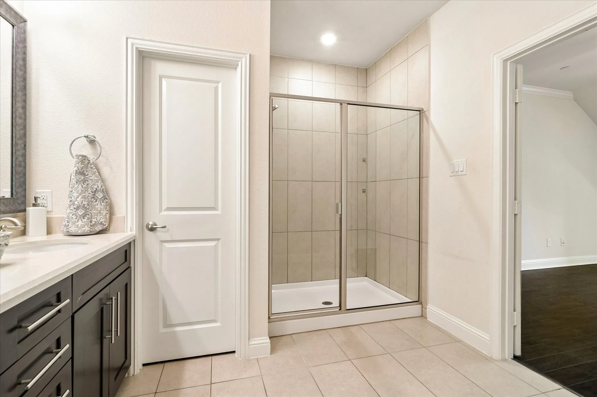 Glass-enclosed shower with tiled walls, dark wood-finish vanity with a light-toned countertop, and tiled flooring