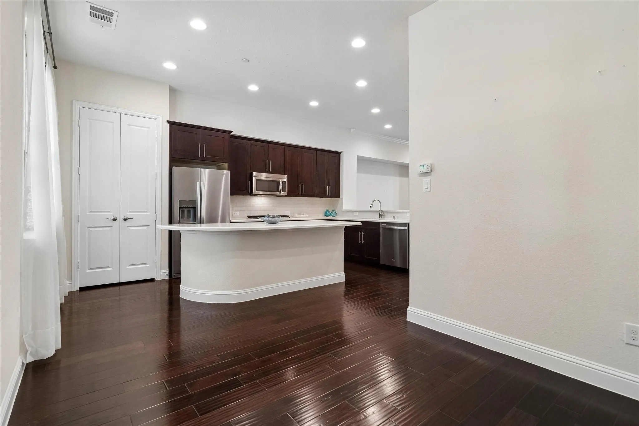 Kitchen featuring dark wood cabinetry, stainless steel appliances, recessed lighting, and a curved peninsula with a light-toned countertop