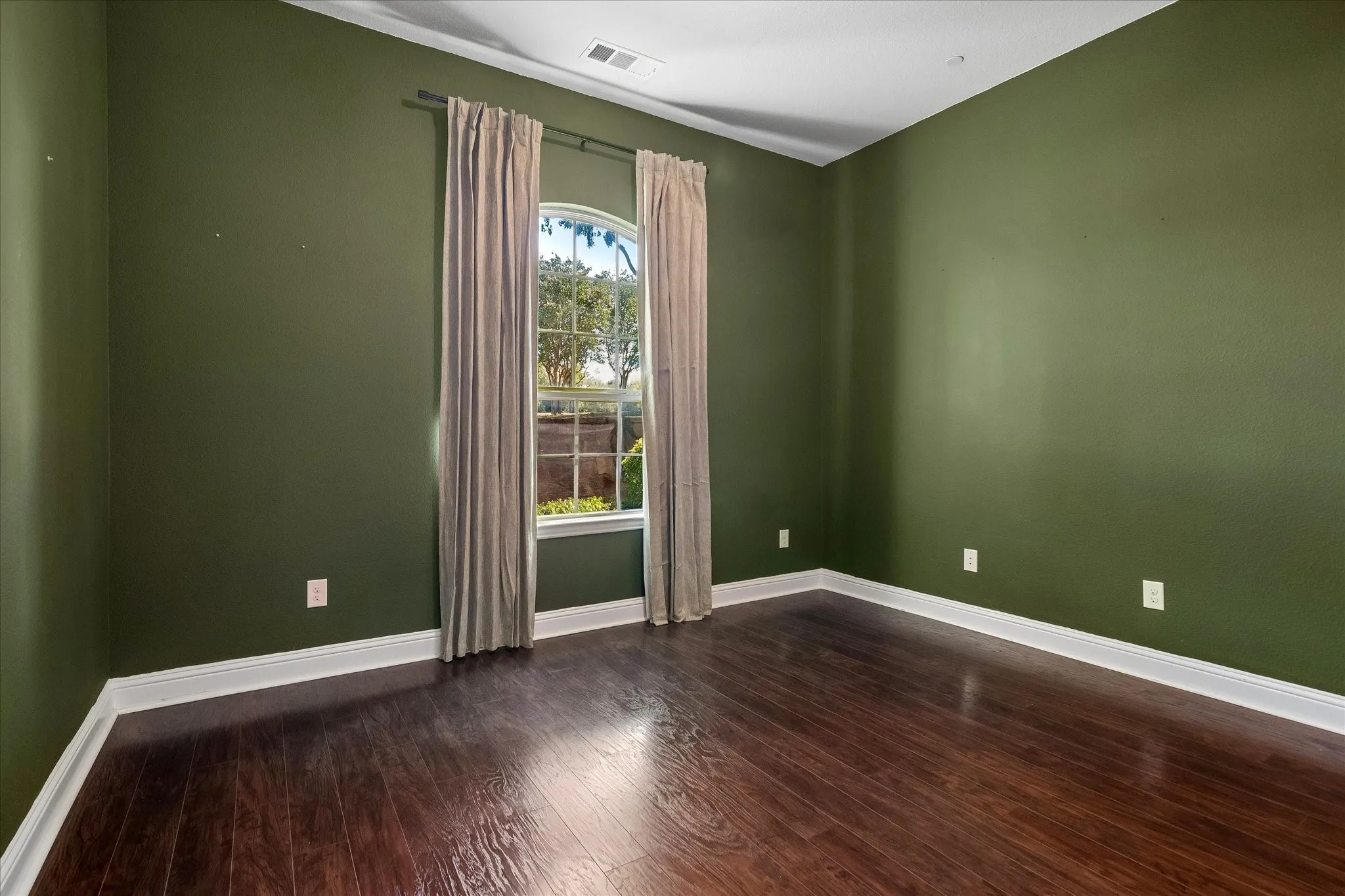 Arched window with exterior landscaping, wood-finish flooring, and white trim