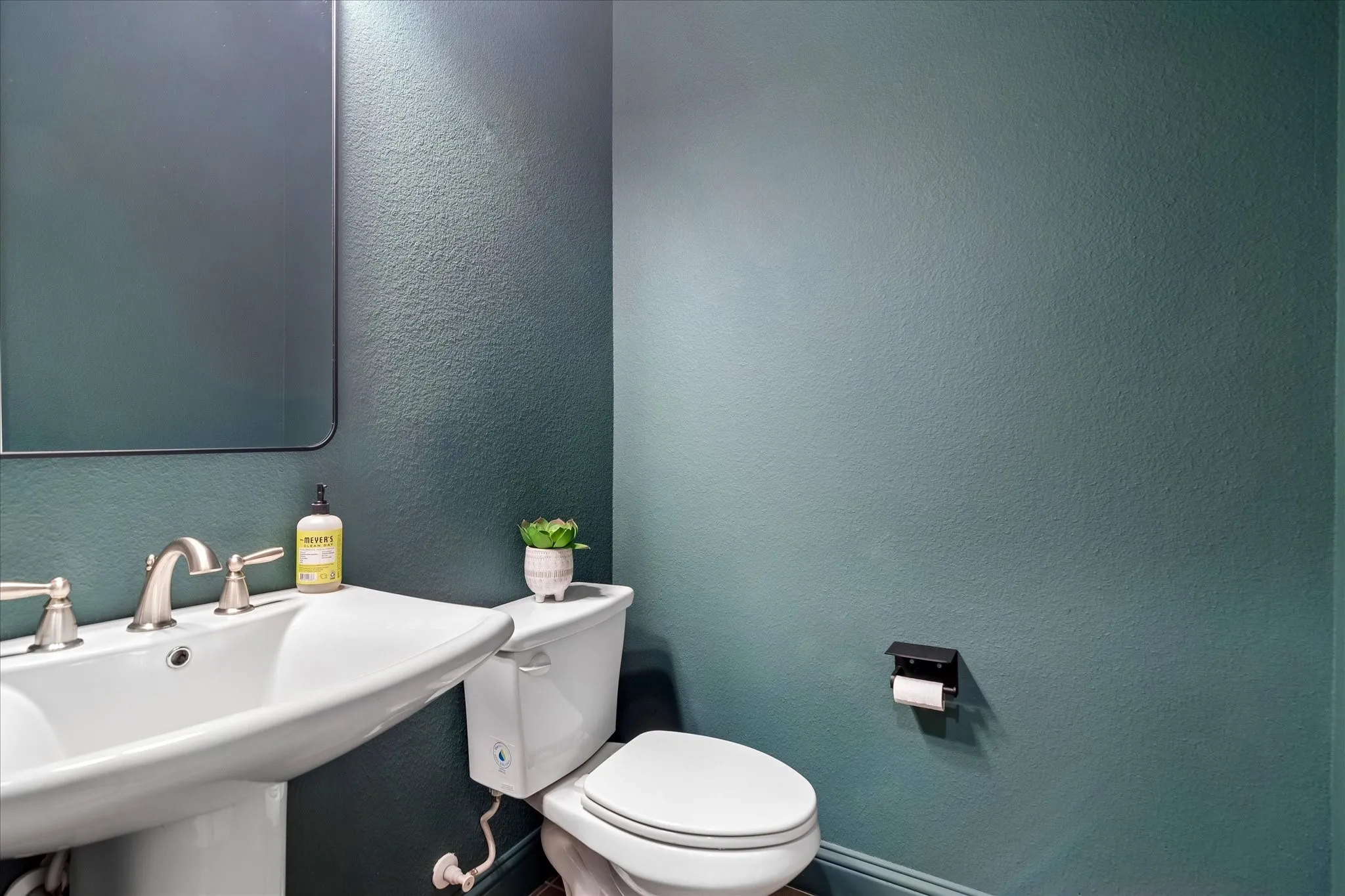 Pedestal sink with brushed nickel faucet, mirror, and toilet