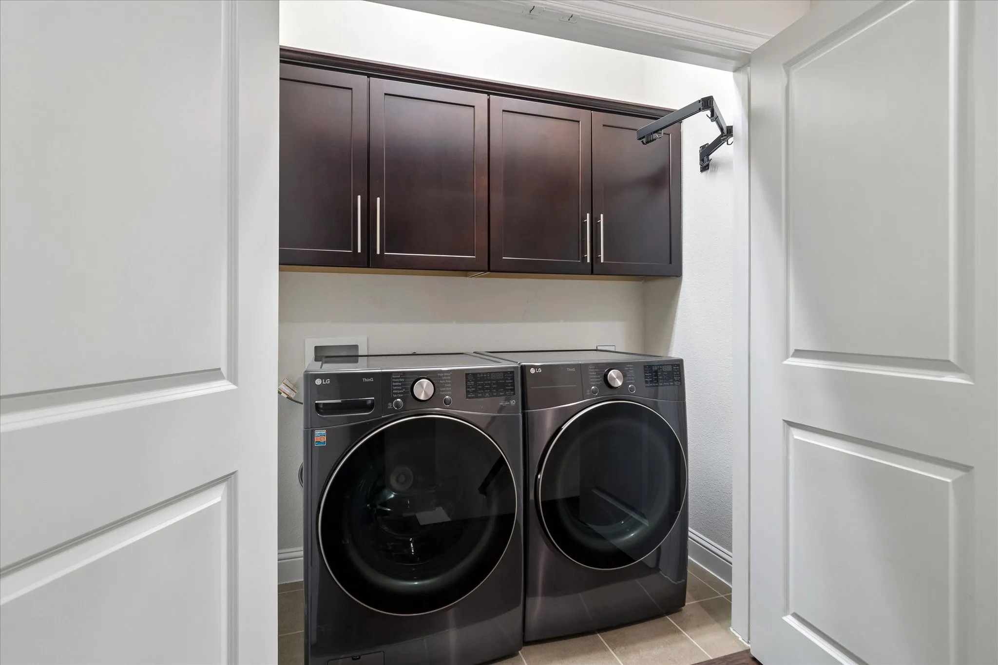 Laundry area featuring dark wood-finish cabinetry, a wall-mounted drying rack, and light-toned floor tiling