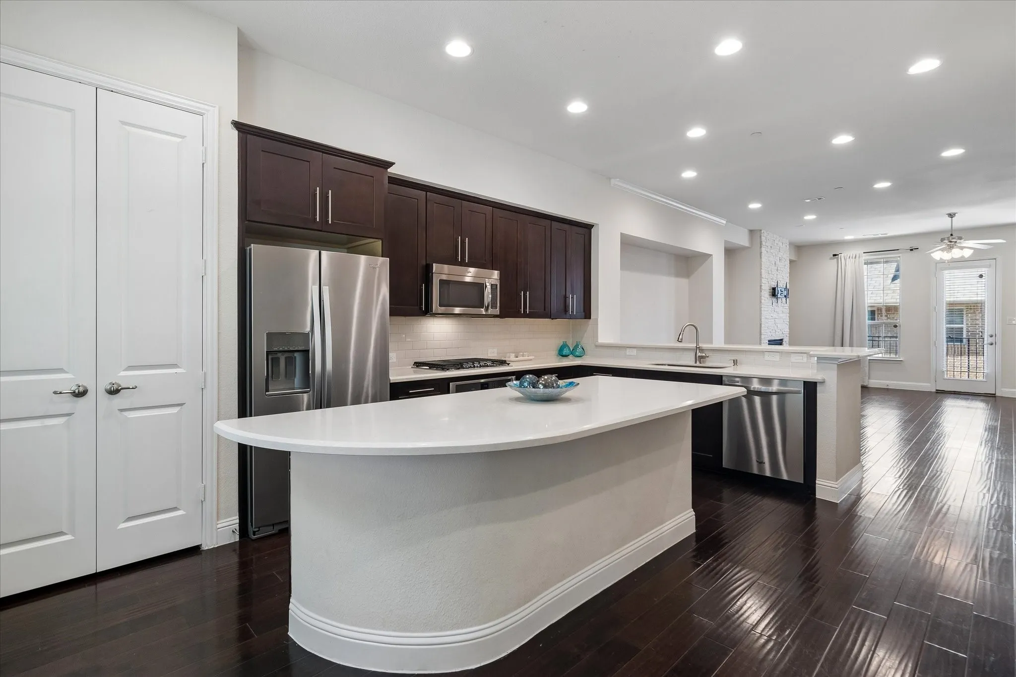Spacious kitchen featuring dark wood cabinetry, stainless steel appliances, a large island with a light-colored countertop, and recessed lighting