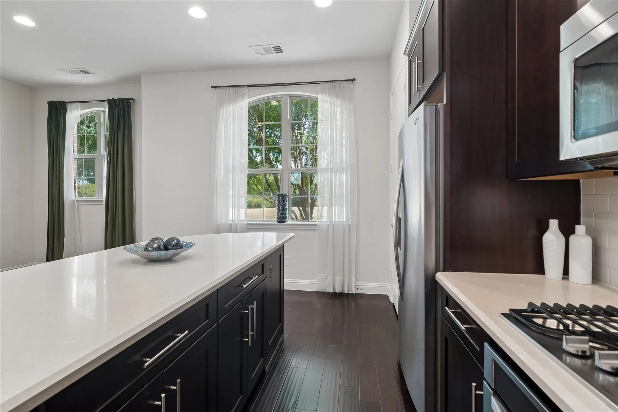 Kitchen featuring a large center island with a light-toned countertop, dark wood-finish cabinetry, stainless steel appliances, and wood-finish flooring