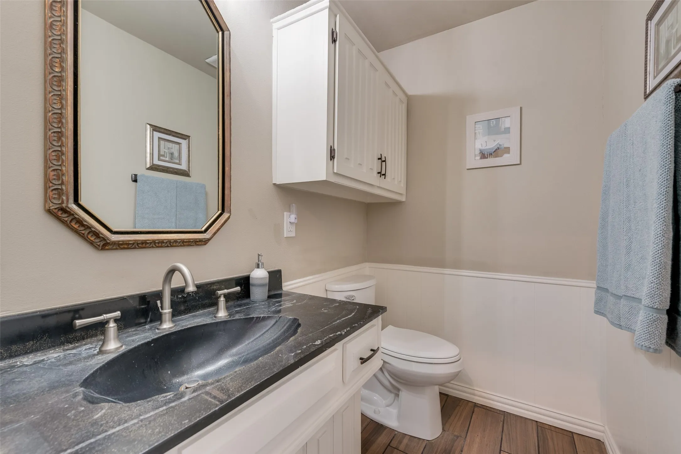 Vanity with stone countertop and integrated sink, brushed nickel faucet, wall-mounted storage cabinet, and wood-finish flooring