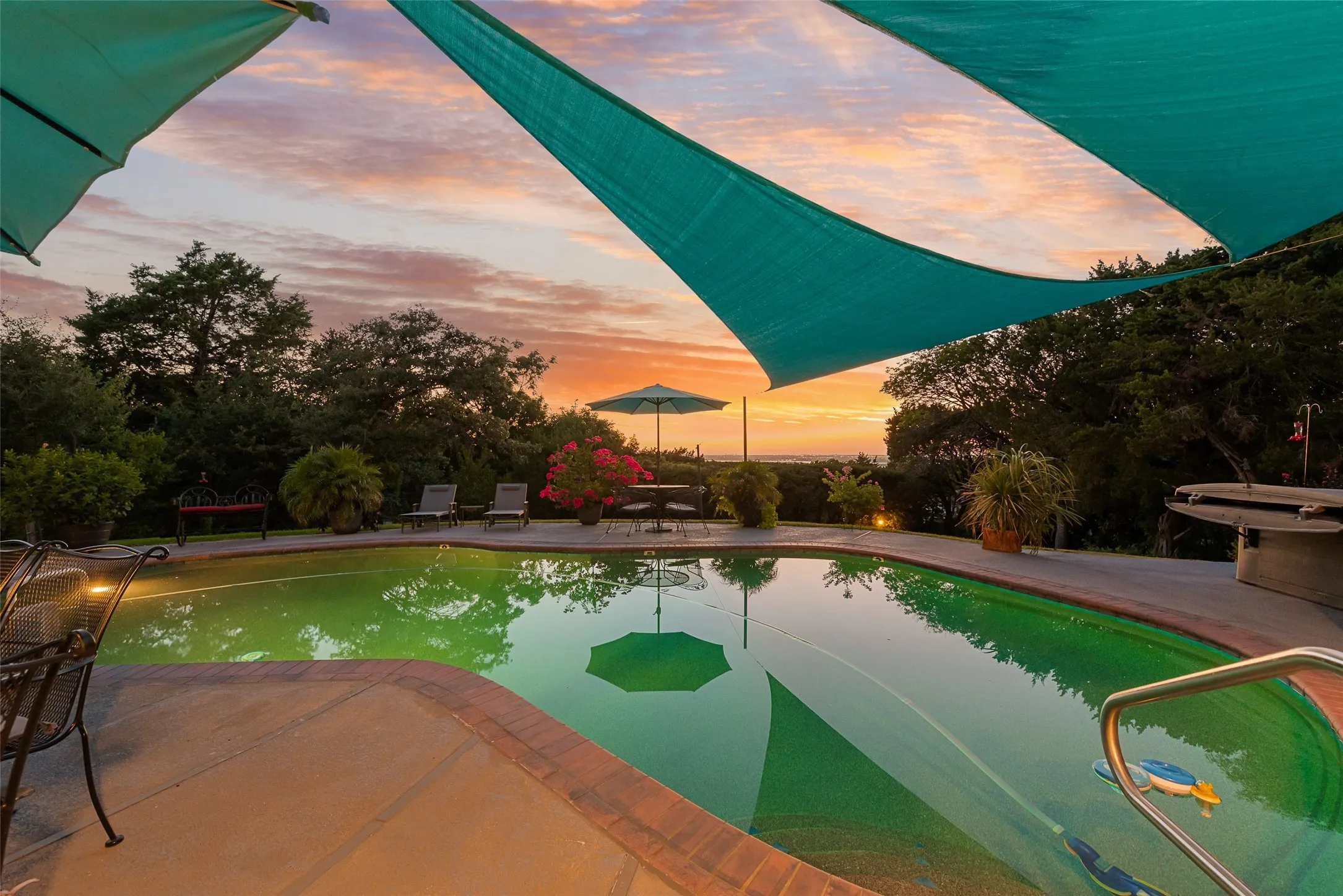 Swimming pool with integrated lighting, concrete pool deck with brick coping, and a metal handrail