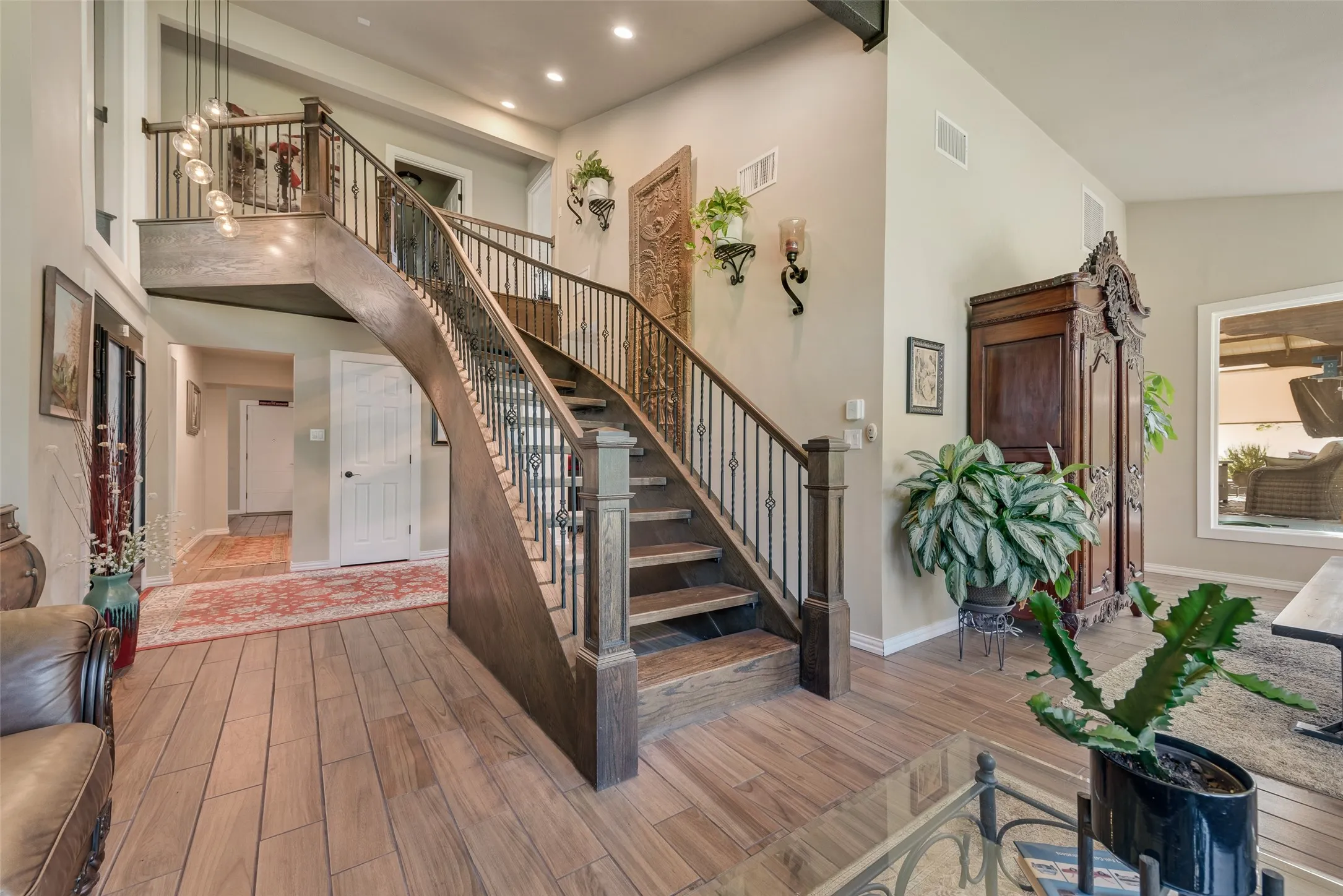 Curved wooden staircase with wrought iron balusters, vaulted ceiling, large windows, and a ceiling fan