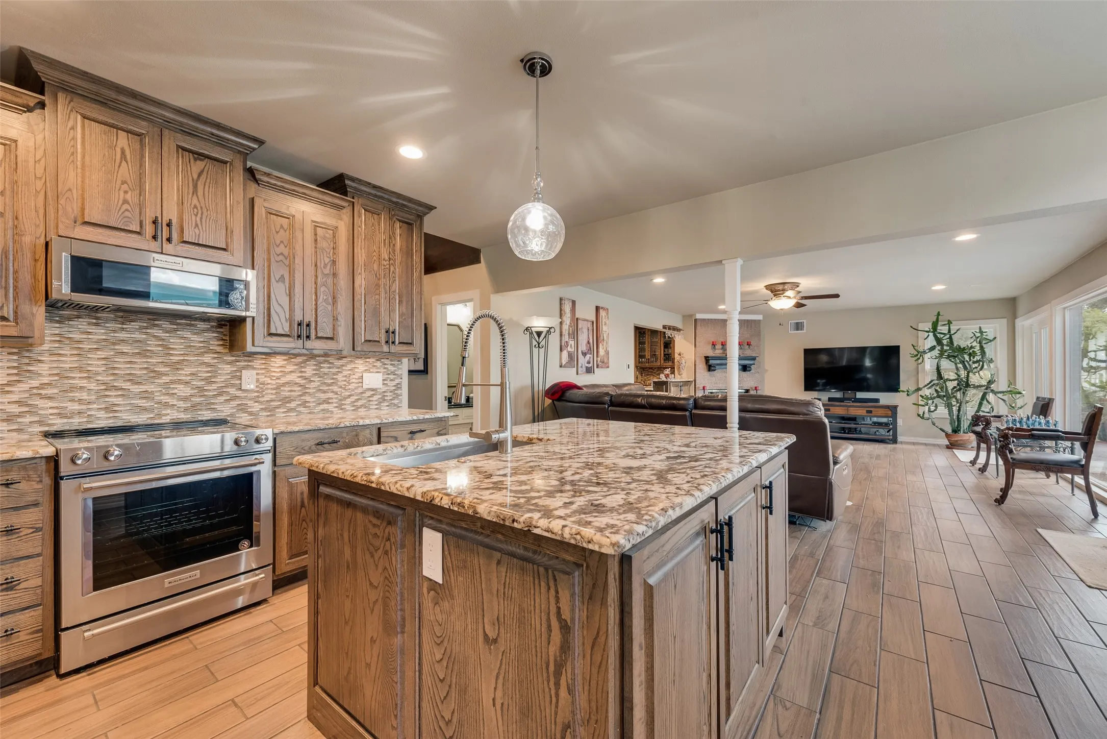 Kitchen featuring wood cabinetry, stainless steel appliances, a tile backsplash, and a central island with a sink and stone countertop