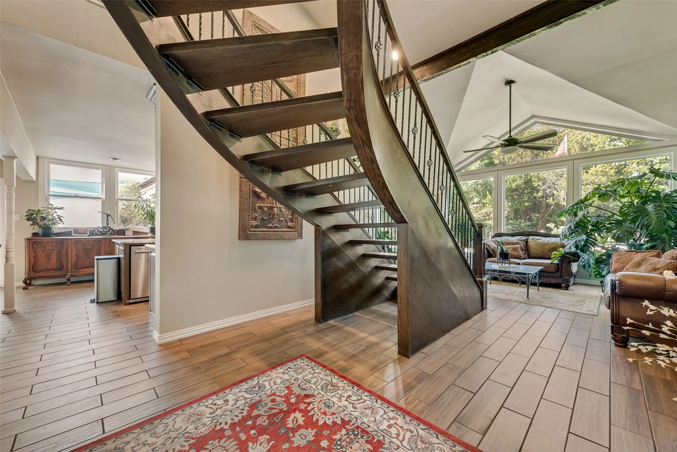 Curved wooden staircase with wrought iron balusters, vaulted ceiling, large windows, and a ceiling fan