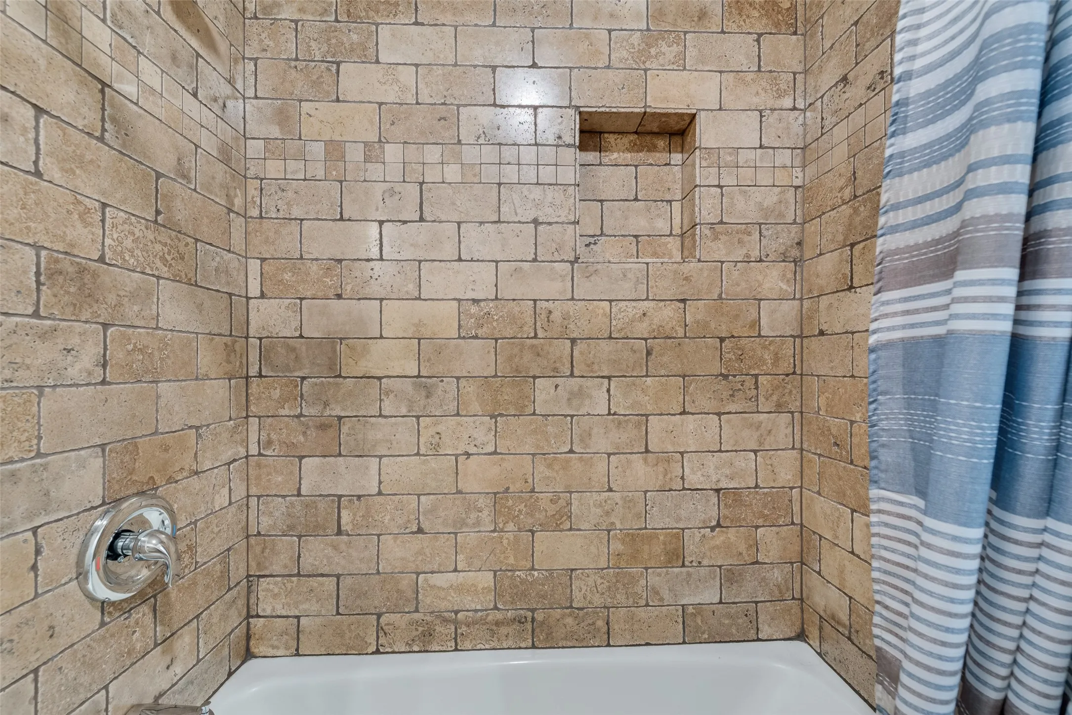Tub/shower combination with natural stone tile surround and a recessed niche