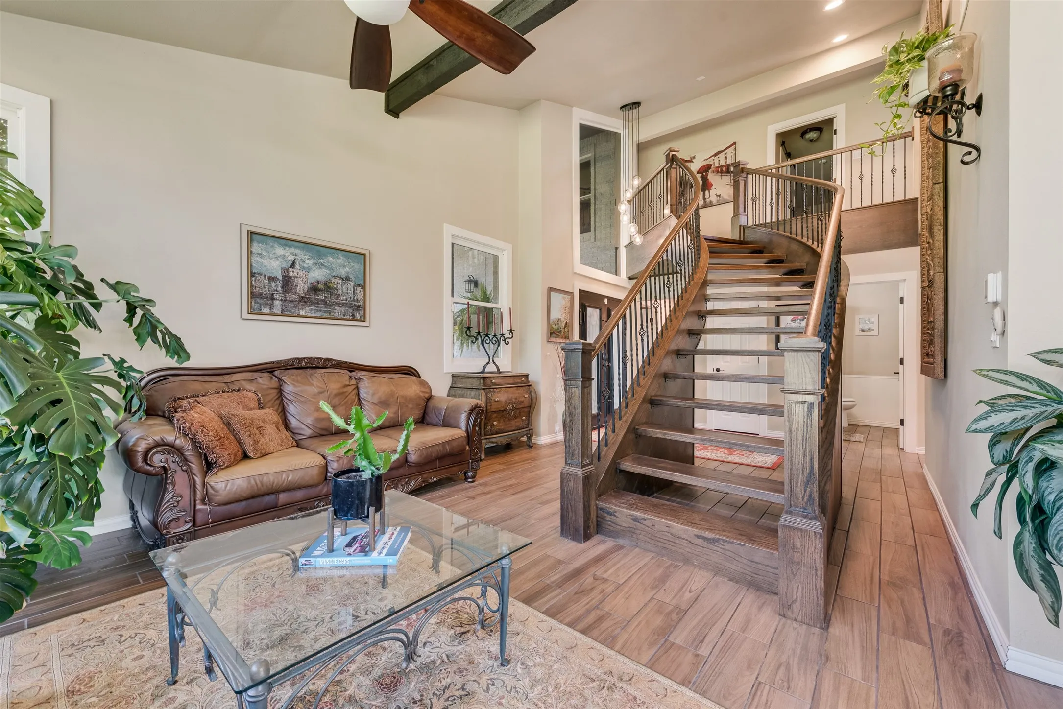 Wood-finish flooring, high ceilings with exposed beams and a ceiling fan, and a curved wooden staircase with wrought iron balusters
