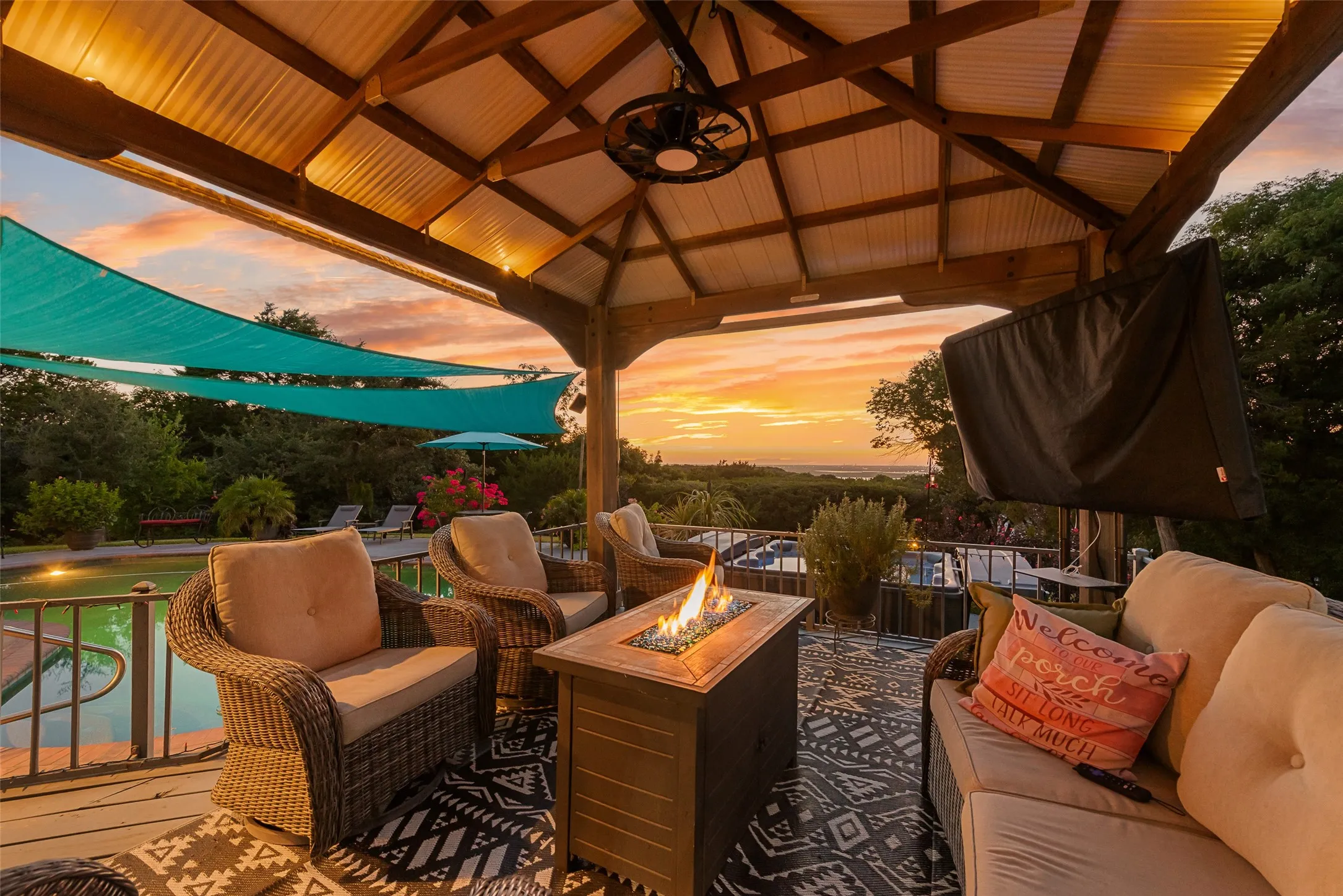 Covered outdoor living space featuring a metal gazebo roof, wood-beam construction, and a ceiling fan