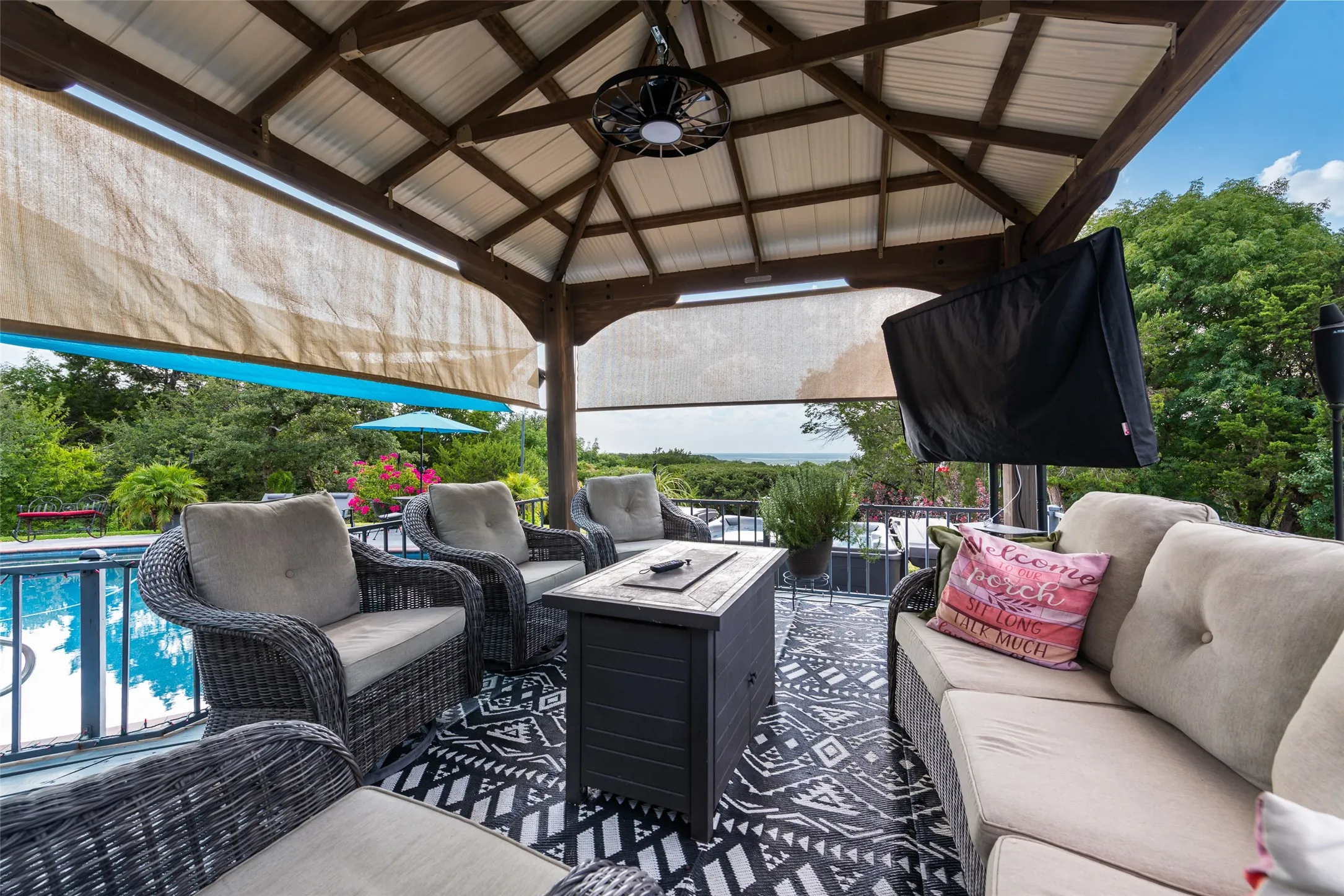 Covered outdoor living space featuring a metal gazebo roof, wood-beam construction, and a ceiling fan