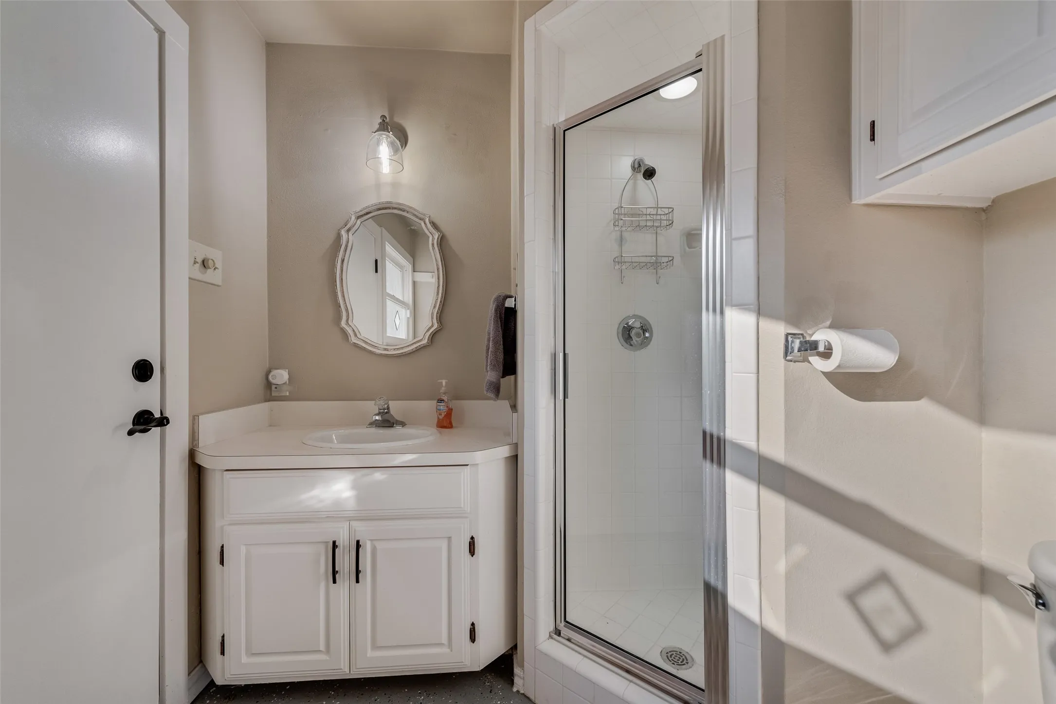 Vanity with integrated sink, glass-enclosed shower, wall-mounted light fixture, and storage cabinetry
