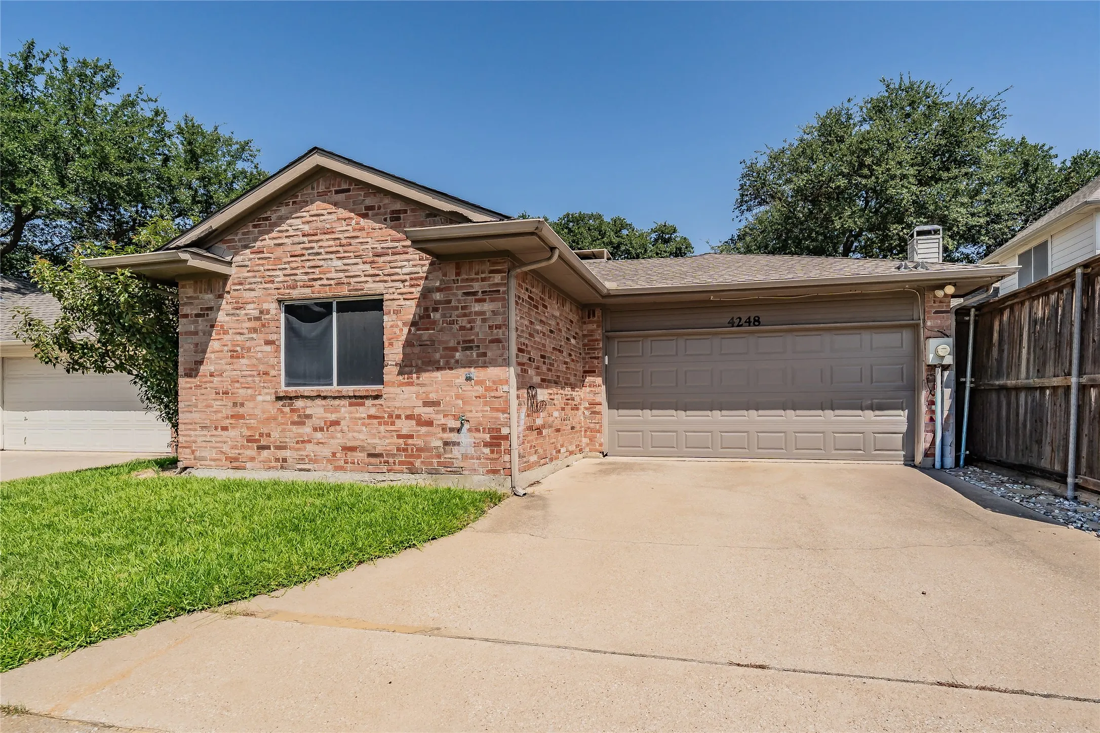 Brick facade residence with an attached garage, paved driveway, and a wood privacy fence