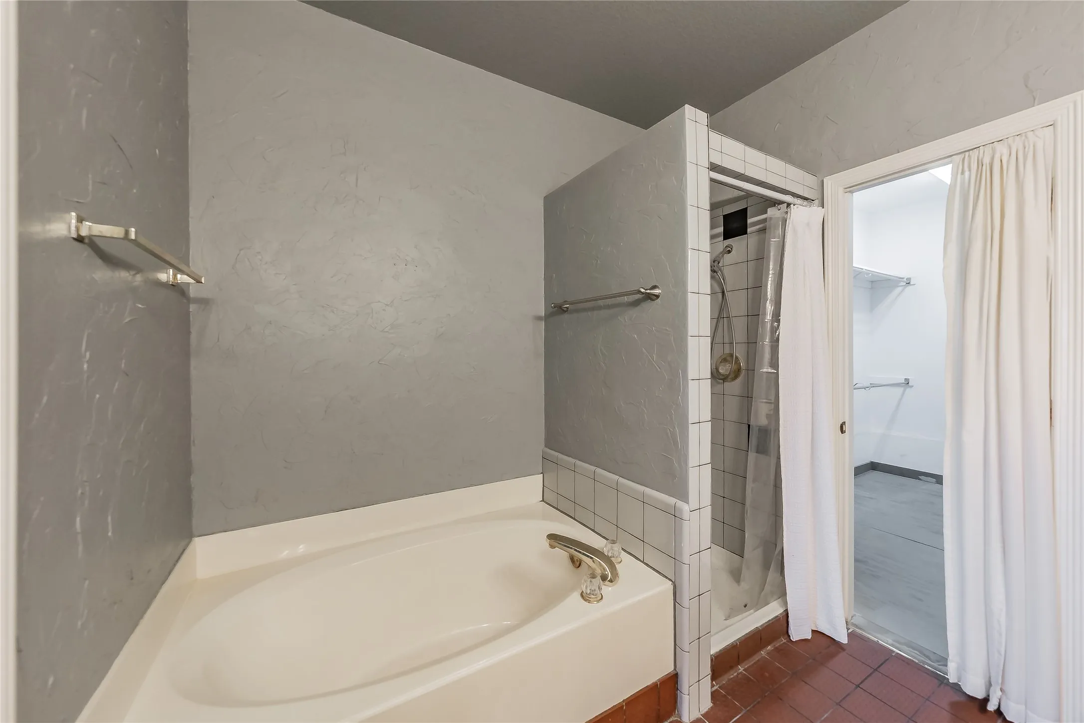 Soaking tub with brass-finish fixtures, a tiled shower enclosure, and terra cotta-style flooring