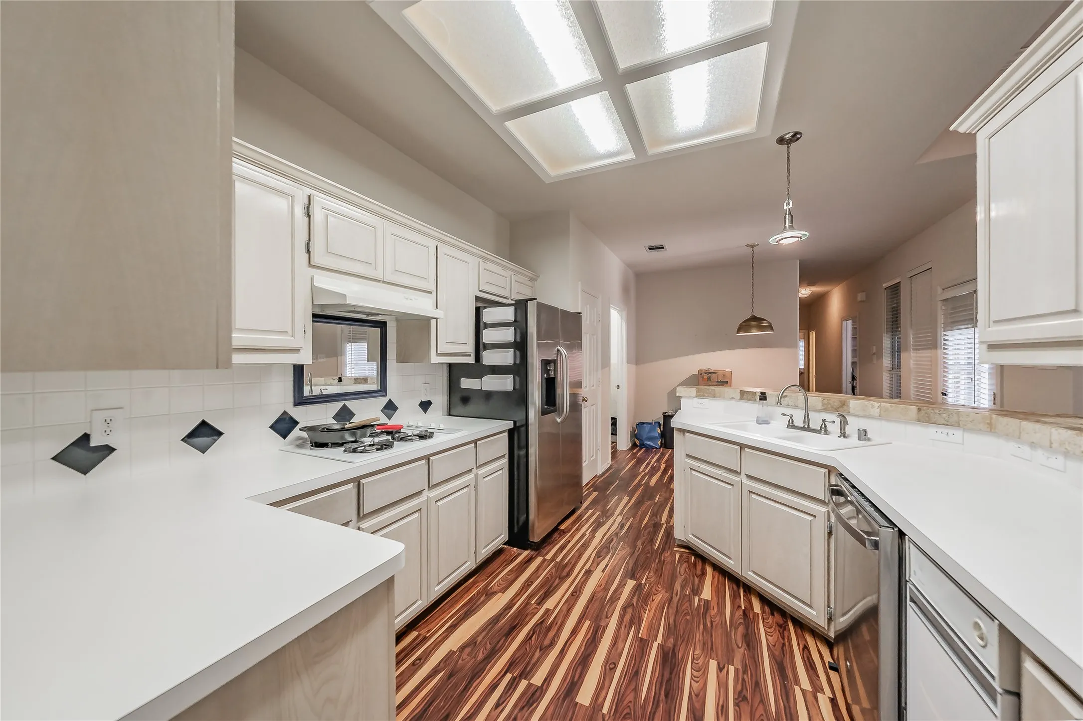 White cabinetry with crown molding, light countertops, wood-finish flooring, stainless steel appliances, and a recessed ceiling light fixture
