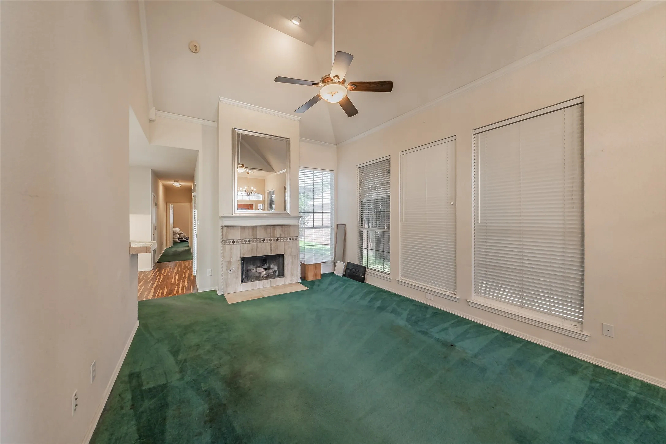 Vaulted ceiling with ceiling fan, tiled fireplace with hearth, and three large windows