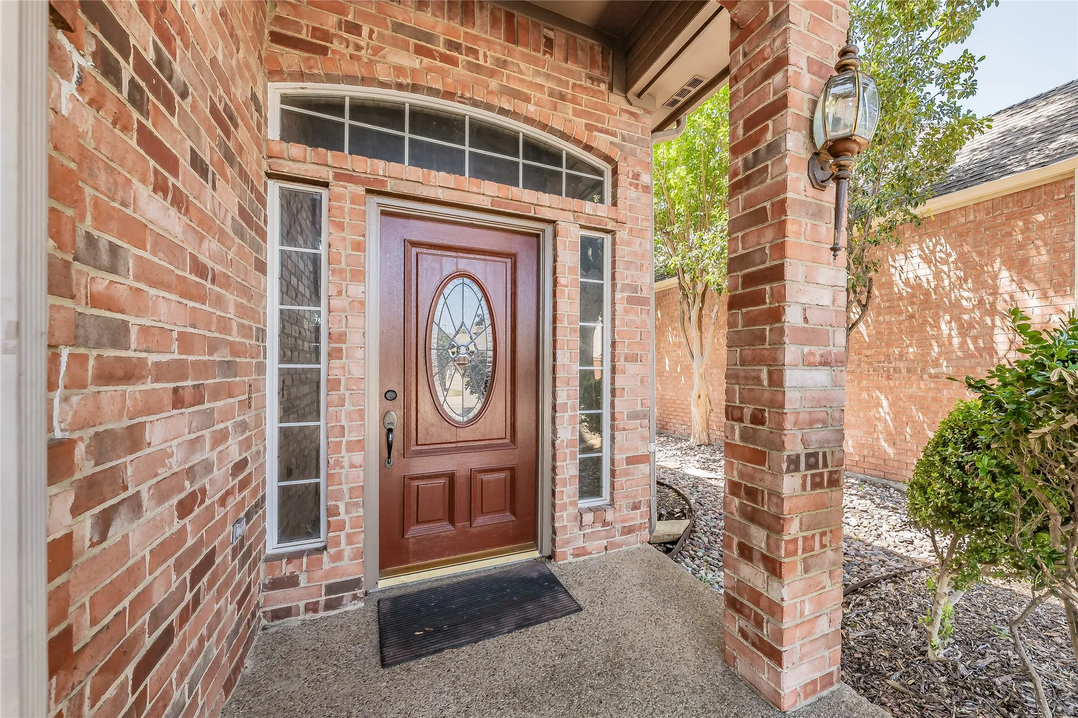 Brick exterior with a covered entry, decorative oval glass door, transom window, and a wall-mounted exterior light fixture
