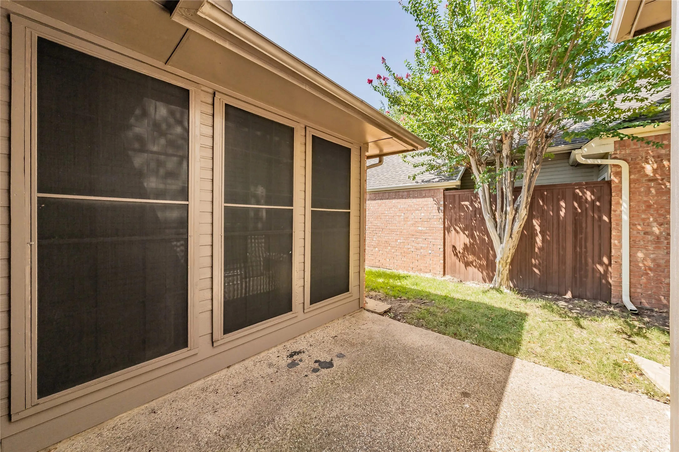Concrete patio with a mature tree, privacy fencing, and brick exterior walls