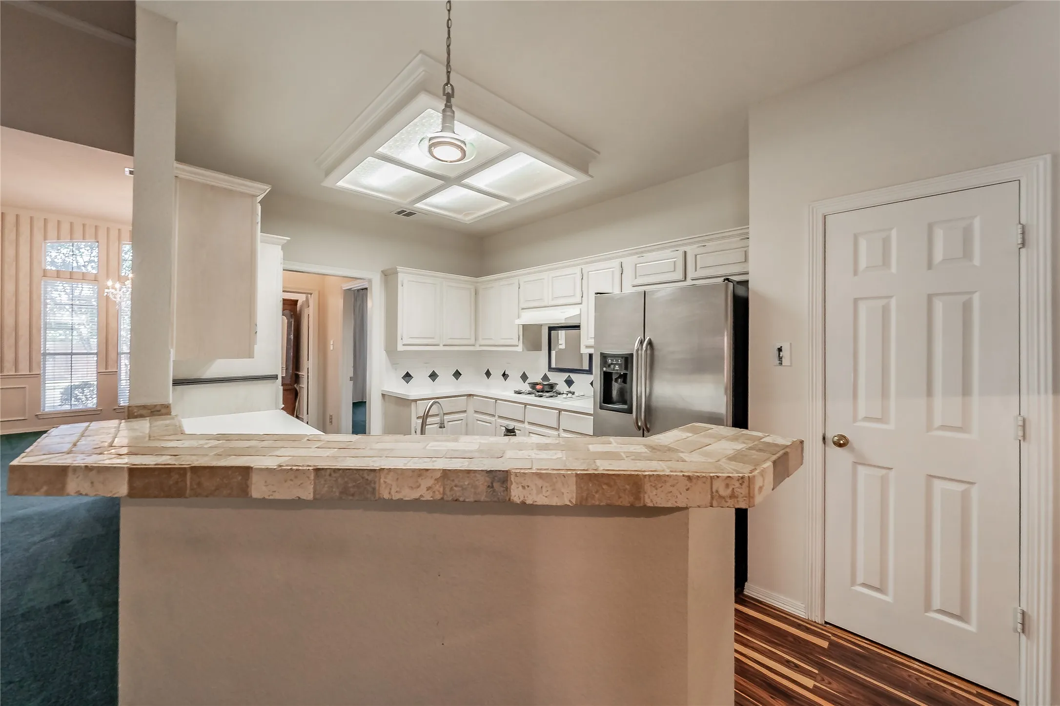 Kitchen featuring white cabinetry, stainless steel refrigerator, tile backsplash, and a tiled breakfast bar