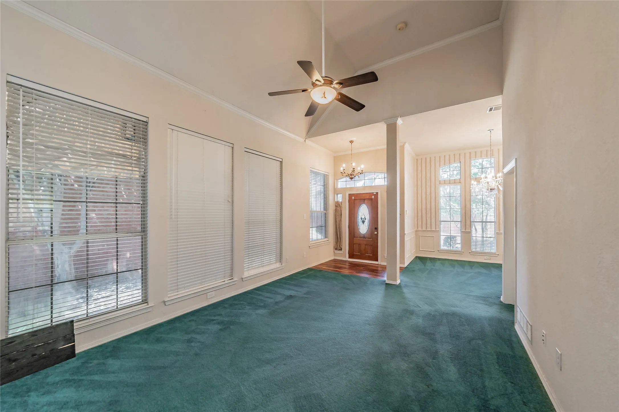 Vaulted ceiling with ceiling fan, multiple large windows, natural wood-finish door with oval glass insert, chandelier lighting, and column architectural elements