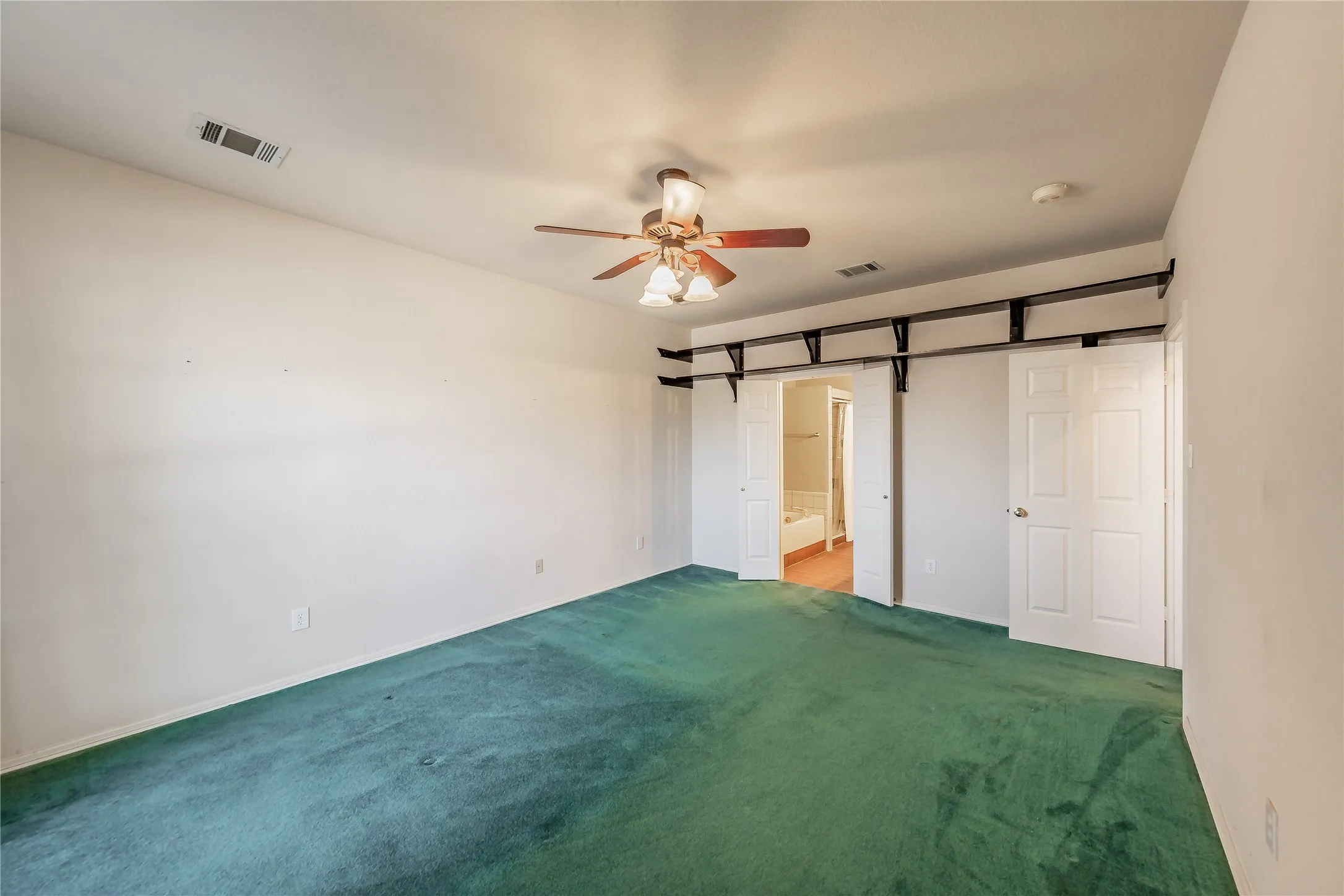 Spacious room featuring broadloom carpeting, a ceiling fan with integrated lighting, and a white interior door