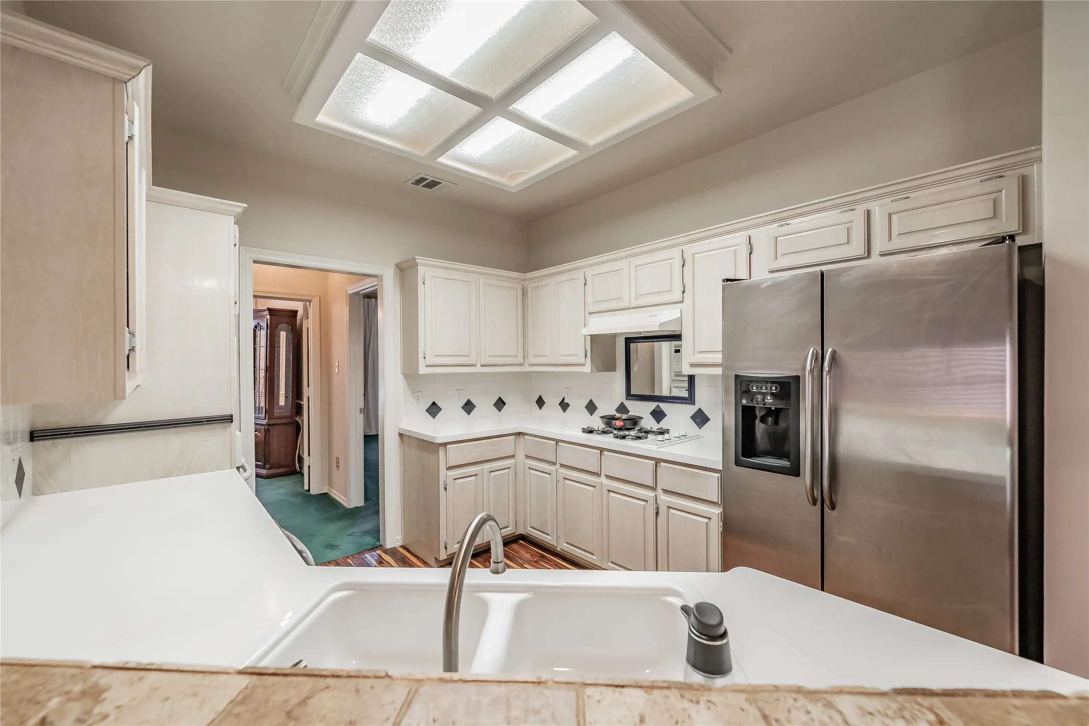 Kitchen featuring abundant white cabinetry, white countertops, stainless steel side-by-side refrigerator, white tile backsplash with black accents, and a ceiling-mounted light fixture