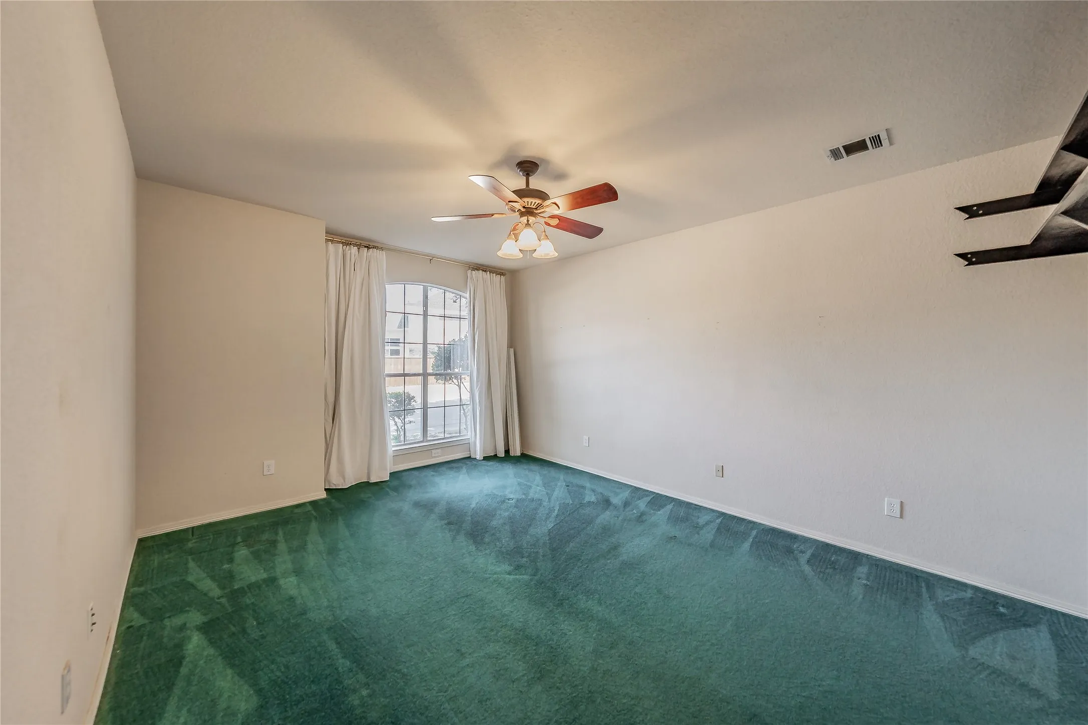 Spacious room featuring a decorative ceiling fan with integrated lighting, wall-to-wall carpeting, and a large window providing ambient light