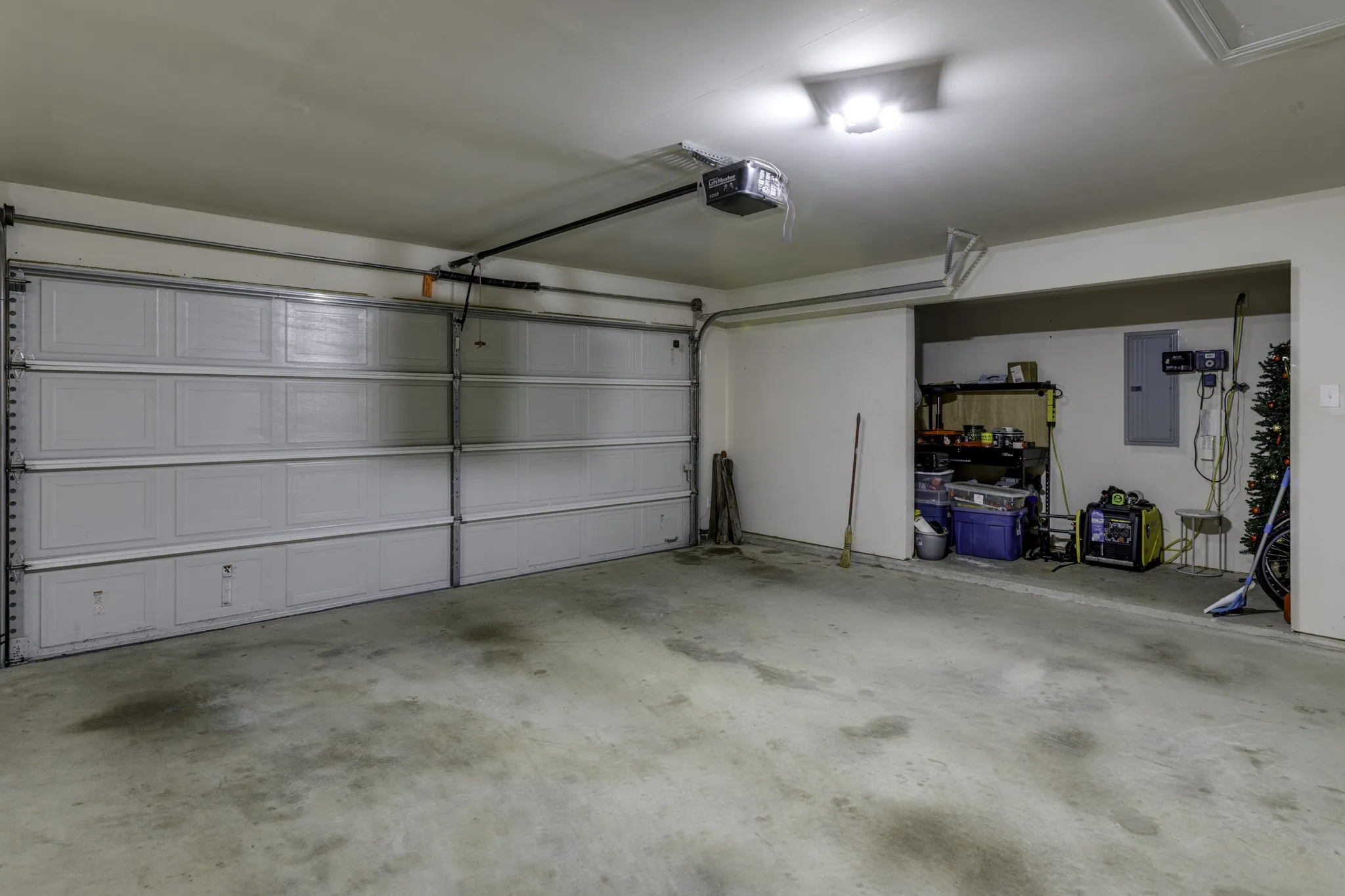 Spacious two-car garage featuring an overhead door with automatic opener, concrete flooring, and extra storage along the side wall