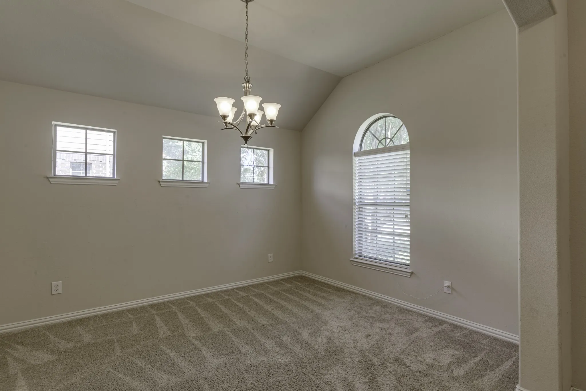 Depending on your lifestyle, this space can be a Living or dining area, featuring a vaulted ceiling, chandelier, arched window with blinds, three rectangular windows, and carpet flooring.