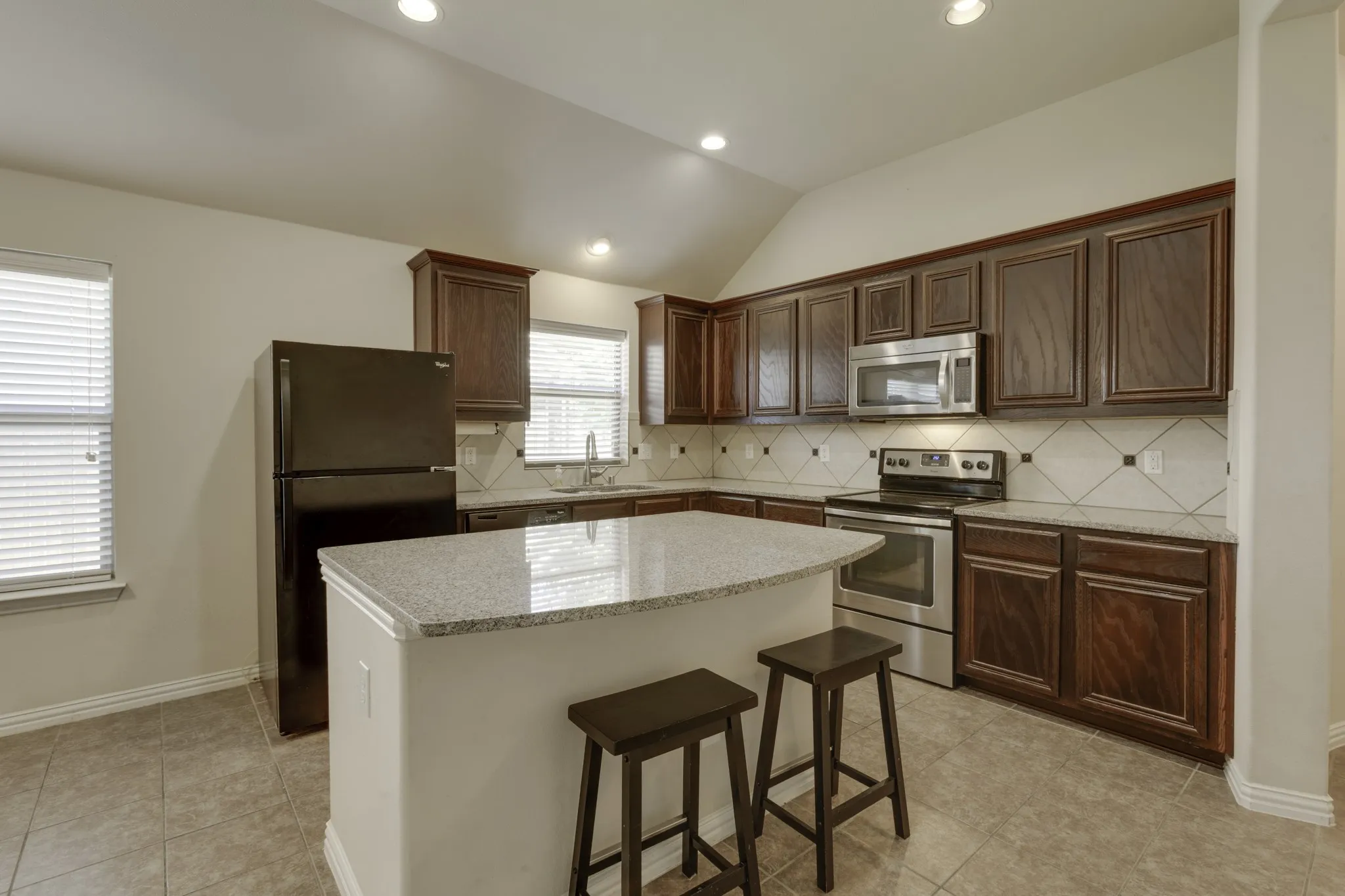 Kitchen featuring dark wood cabinetry, light-toned granite countertops, stainless steel appliances, a tile backsplash, and recessed lighting