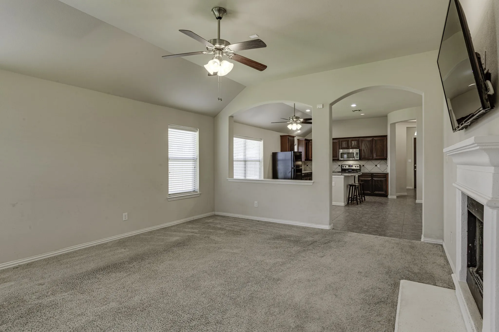 Spacious living area with neutral carpet flooring, ceiling fan with integrated lighting, and a fireplace with white surround