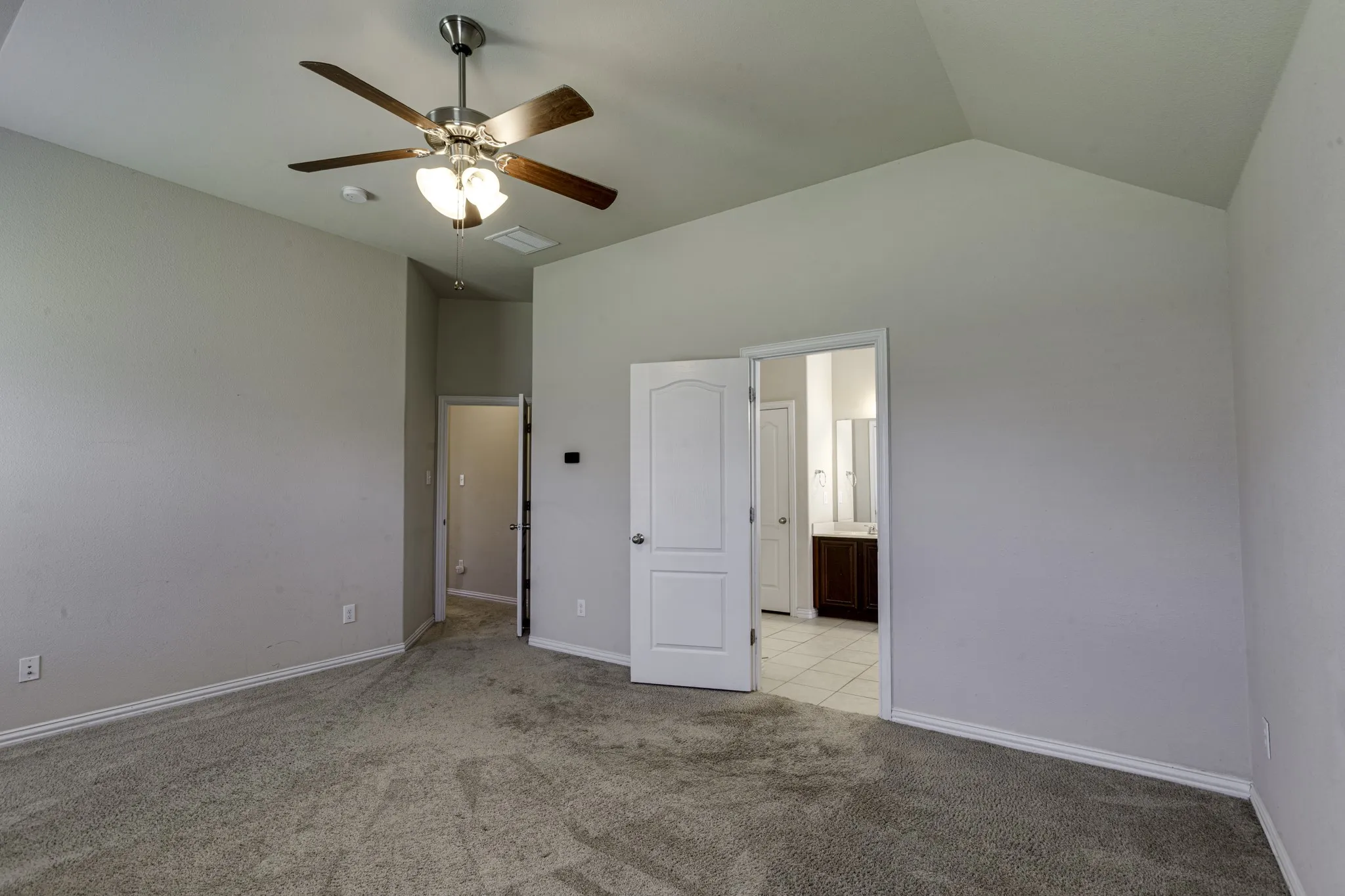 Spacious master bedroom featuring vaulted ceilings, carpeted flooring, ceiling fan with integrated lighting.